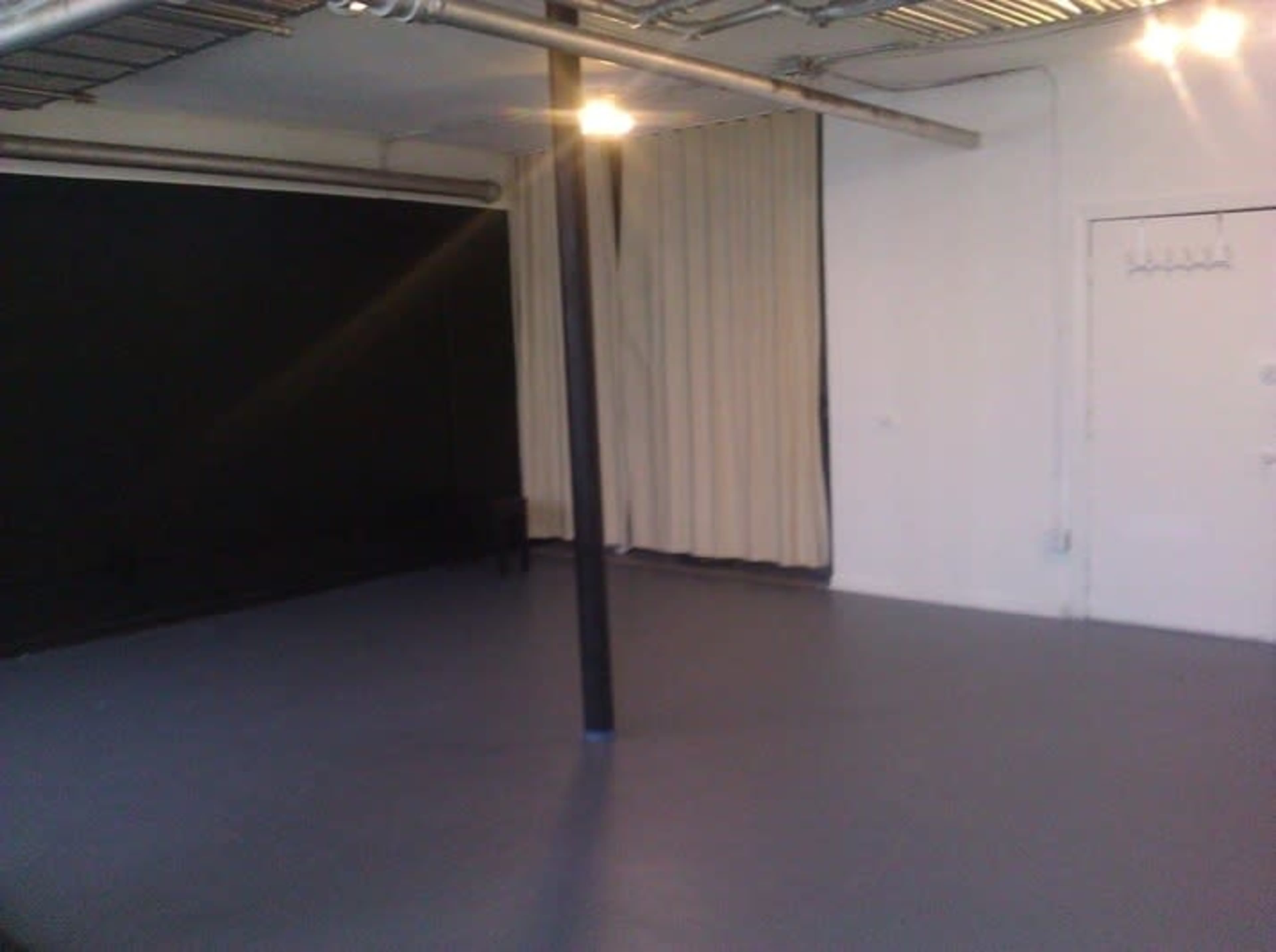 An empty studio space with a gray floor, a black wall, and curtains along one side.