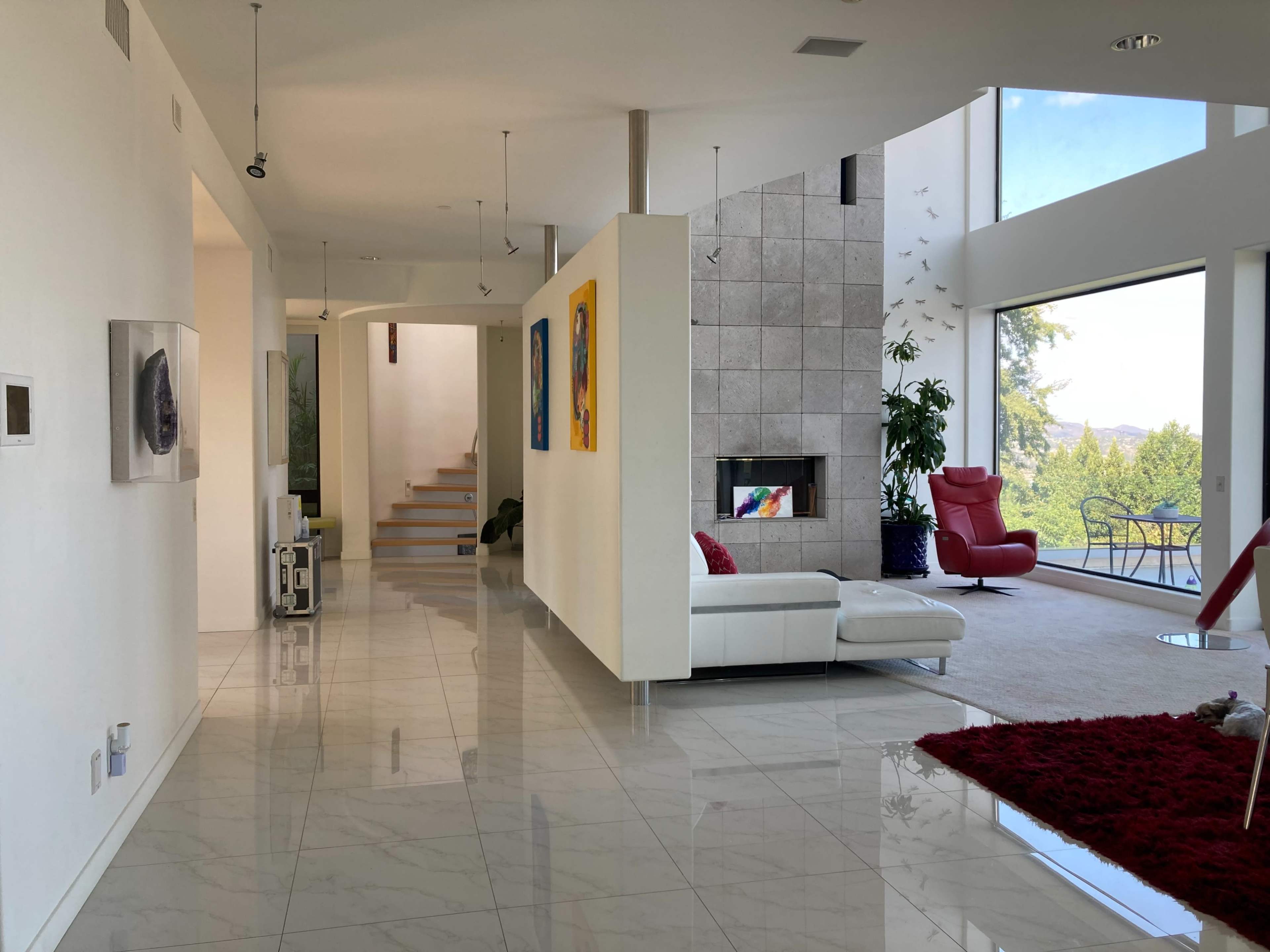 A modern interior space featuring a bright living area with a white sectional sofa, large windows, and a staircase leading to an upper level.