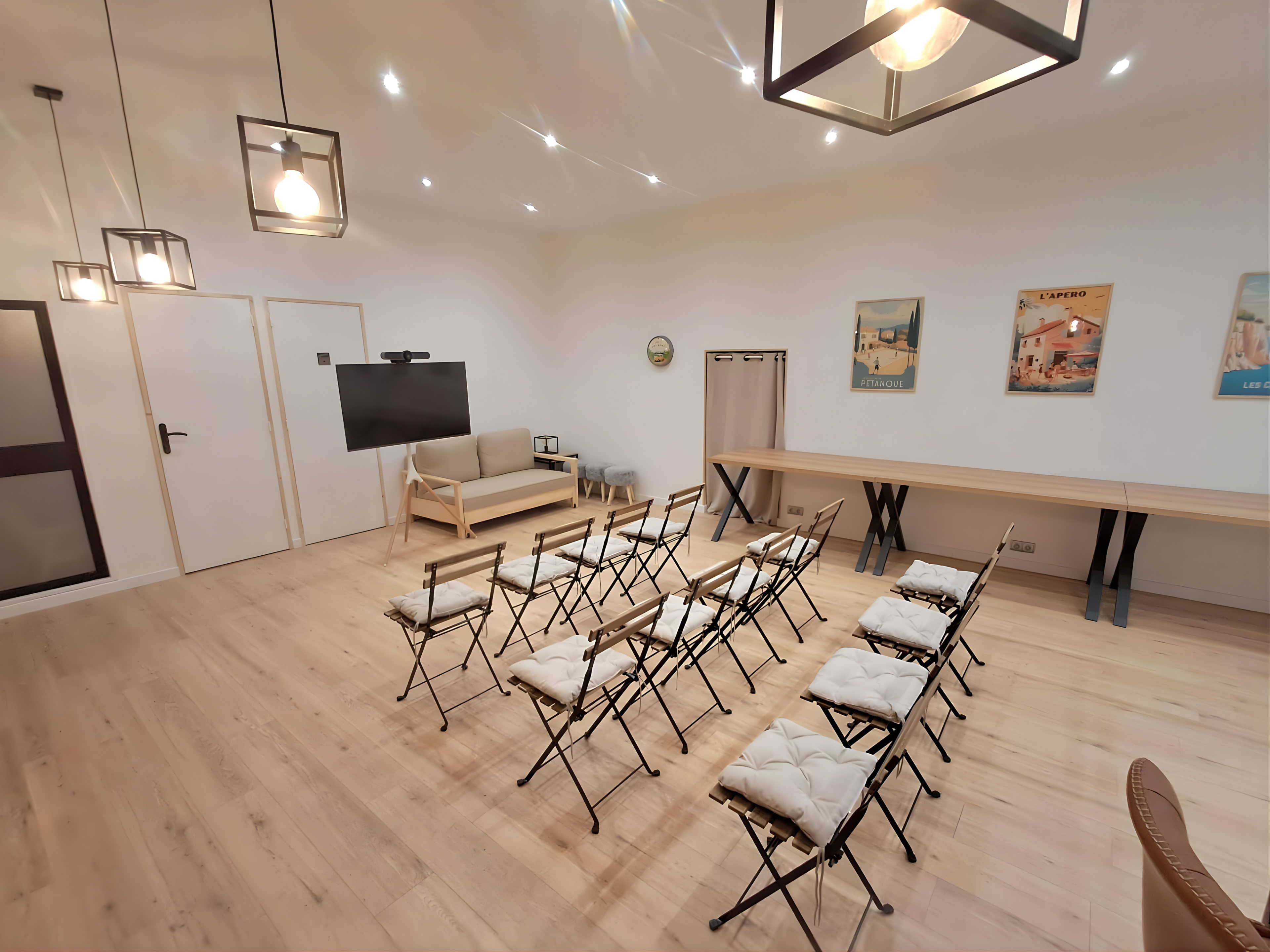 The image shows a well-lit room set up with a row of folding chairs facing a television, with a couch and table against the wall.