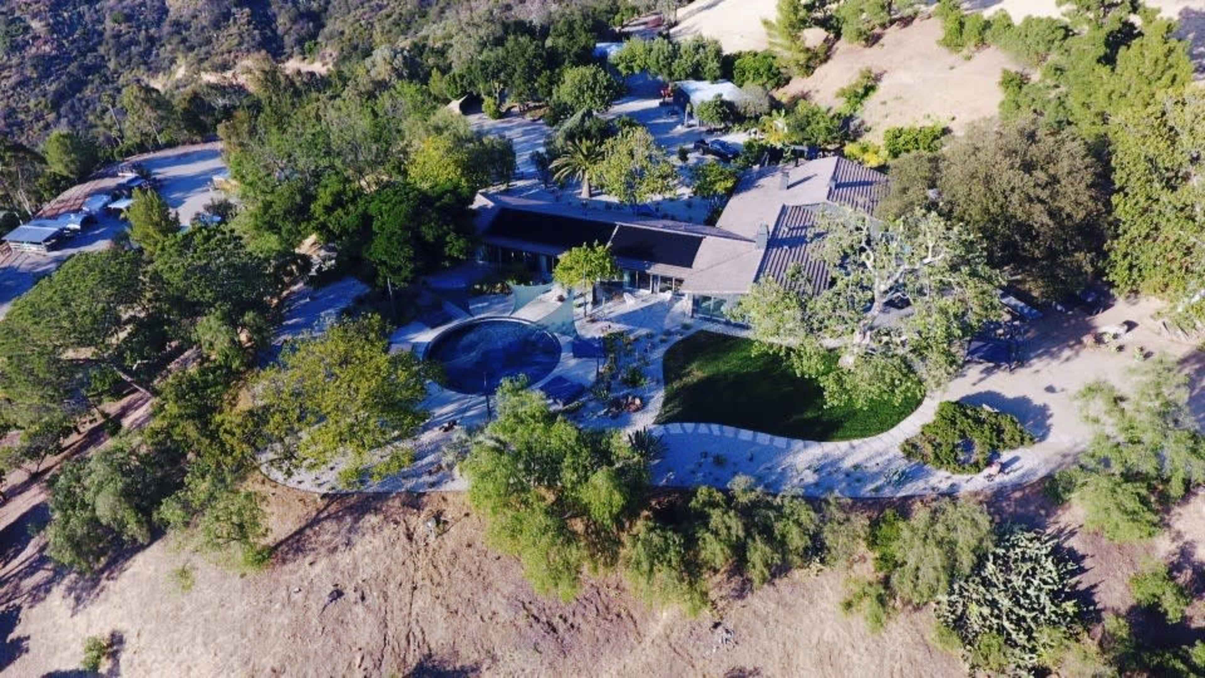 Aerial view of a modern house surrounded by greenery and a circular swimming pool.