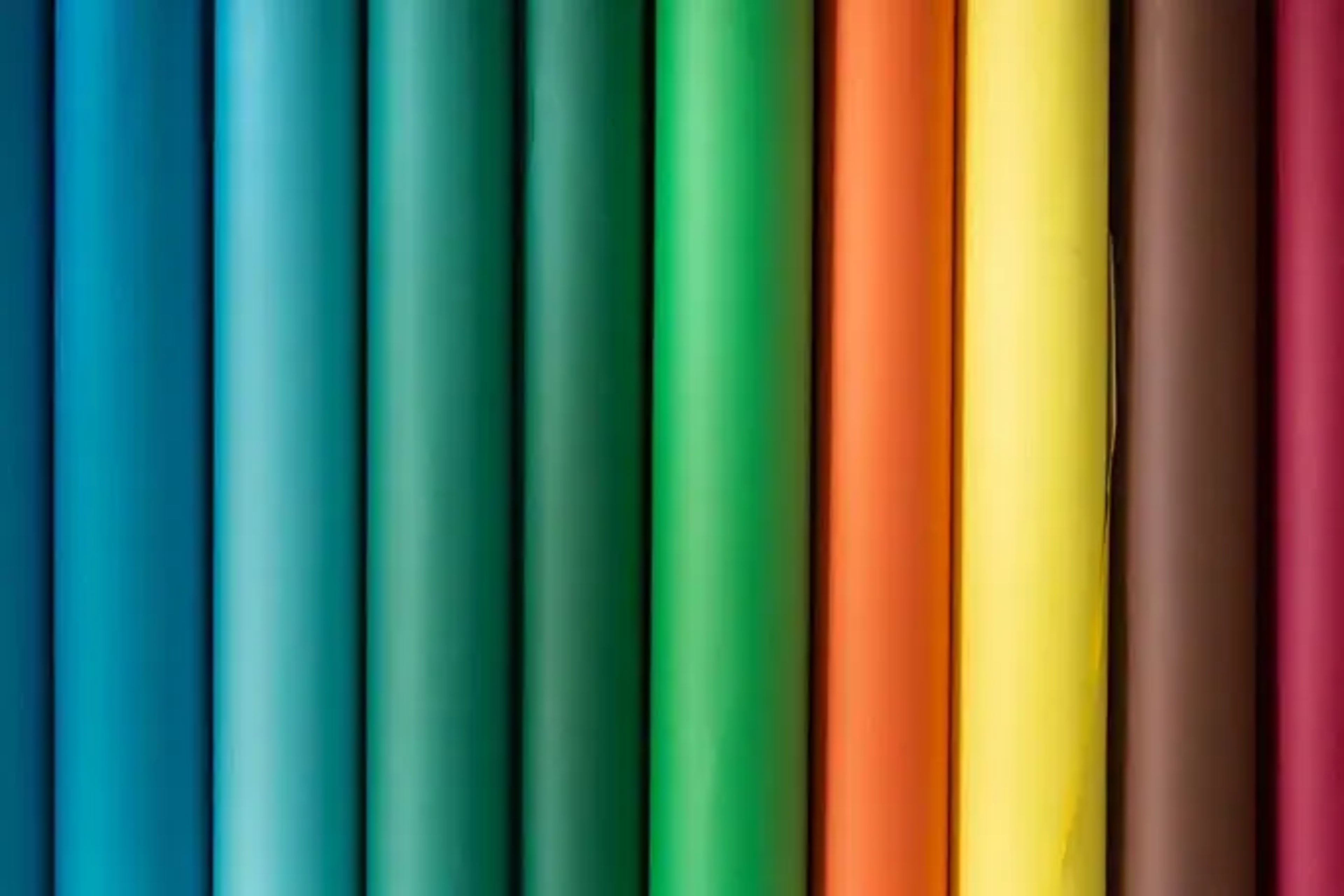 The image shows a collection of vertical rolls of colored paper arranged in a row, featuring bright hues including blue, green, orange, yellow, and brown.