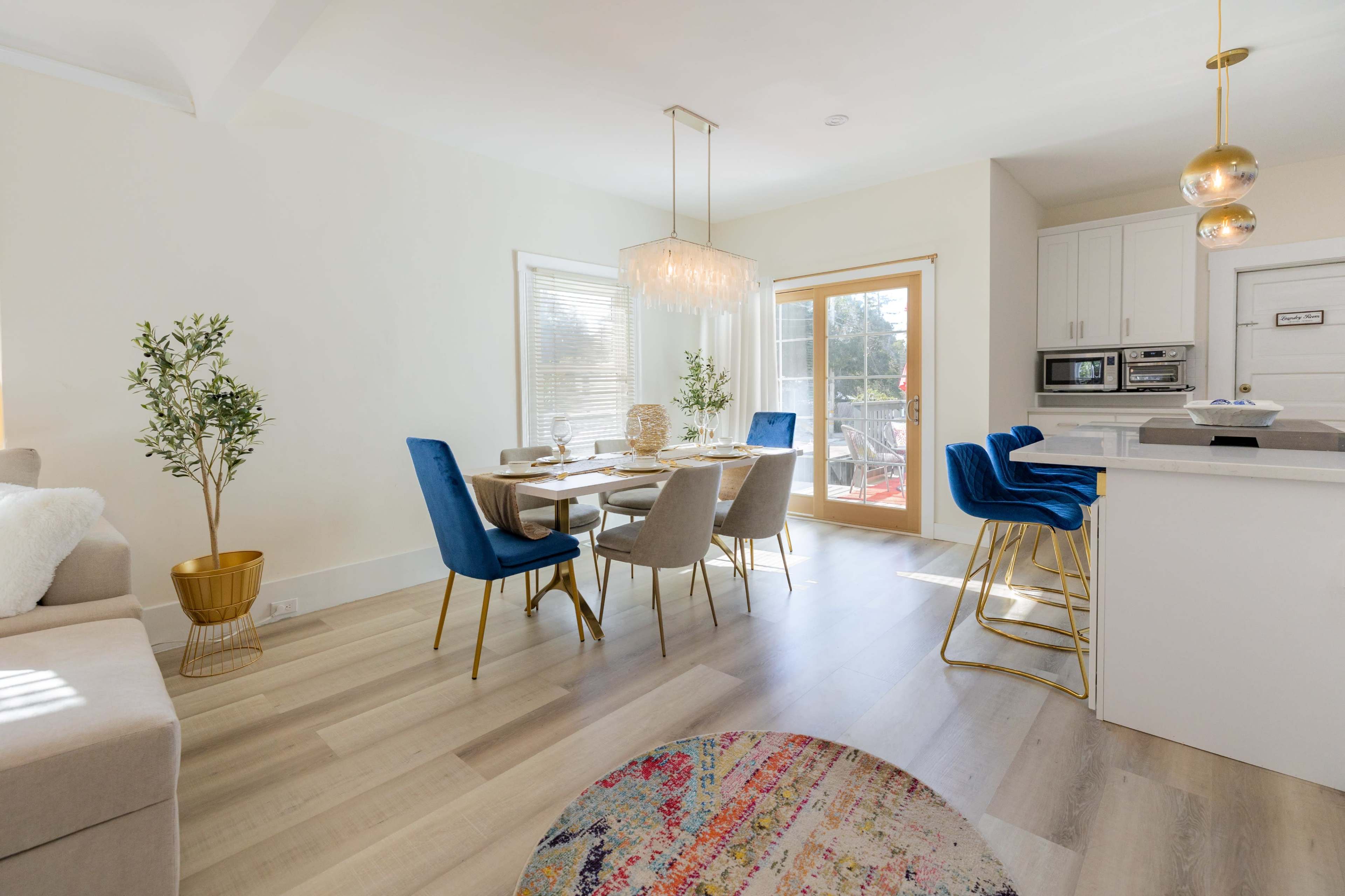 A modern dining area features a table set for six, surrounded by blue and gray chairs, with a sliding glass door leading to an outdoor space.