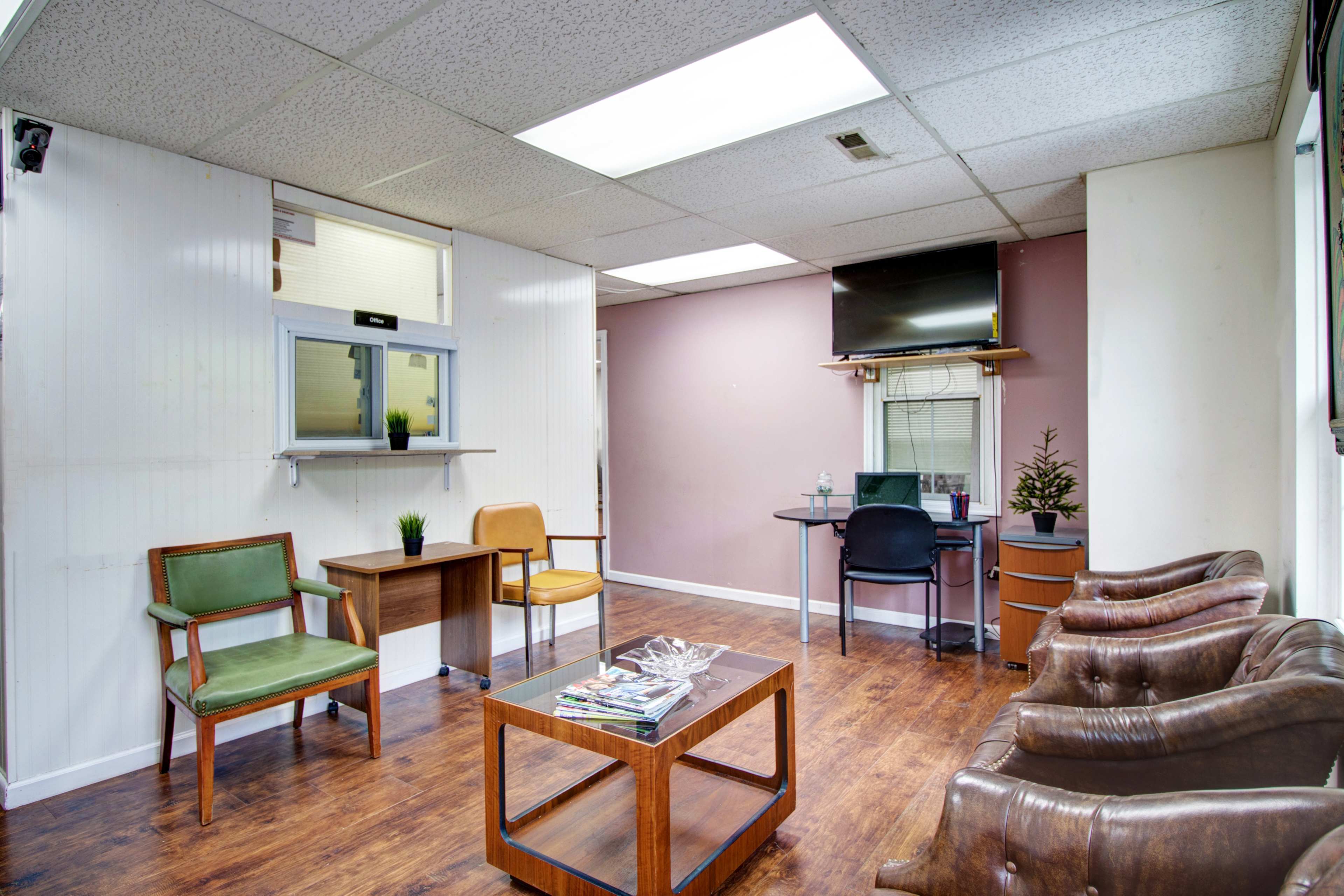 A simple office waiting area with a desk, chairs, and decorative plants.