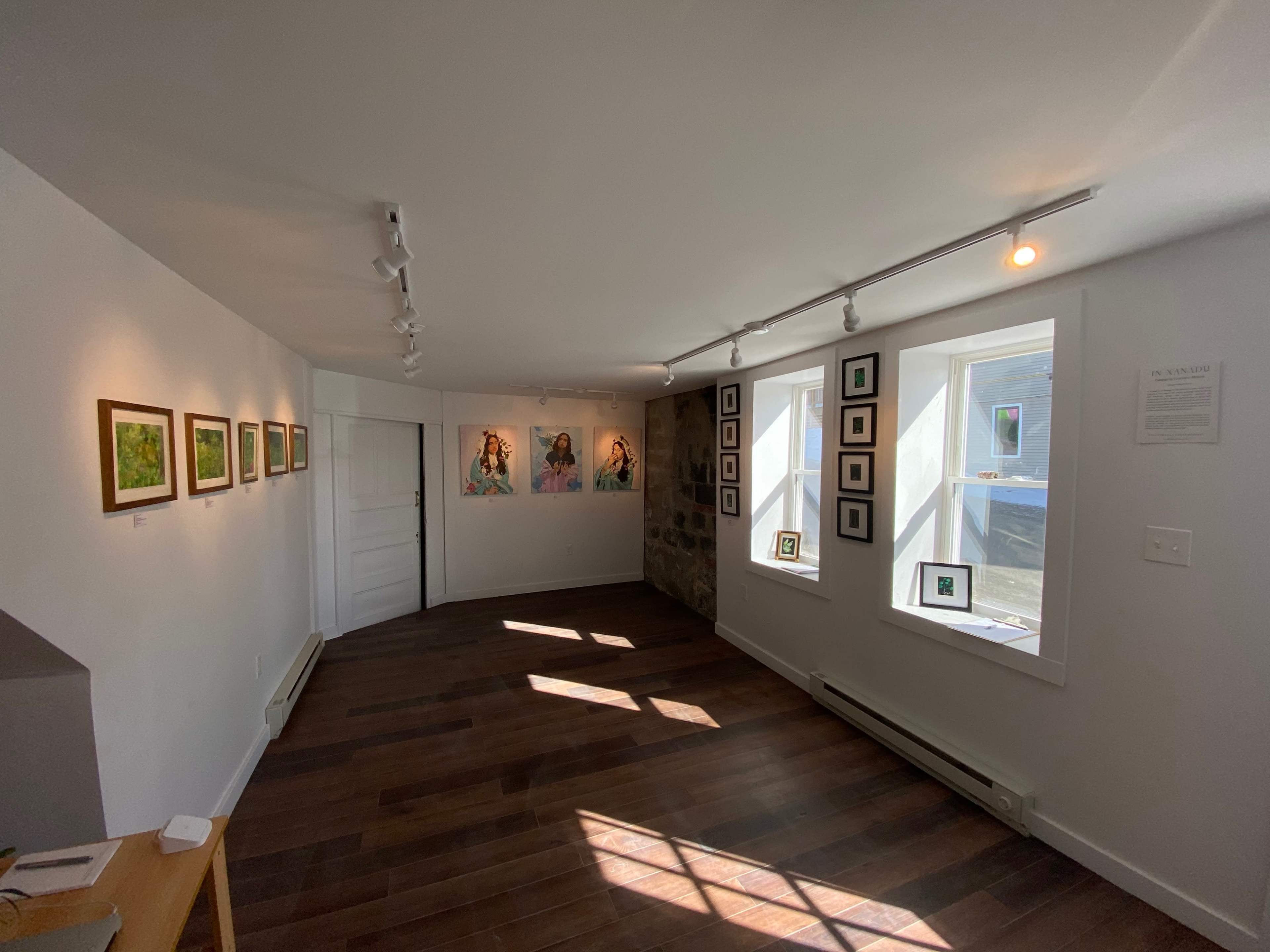An art gallery with framed paintings on the walls and a few small artworks displayed on shelves.
