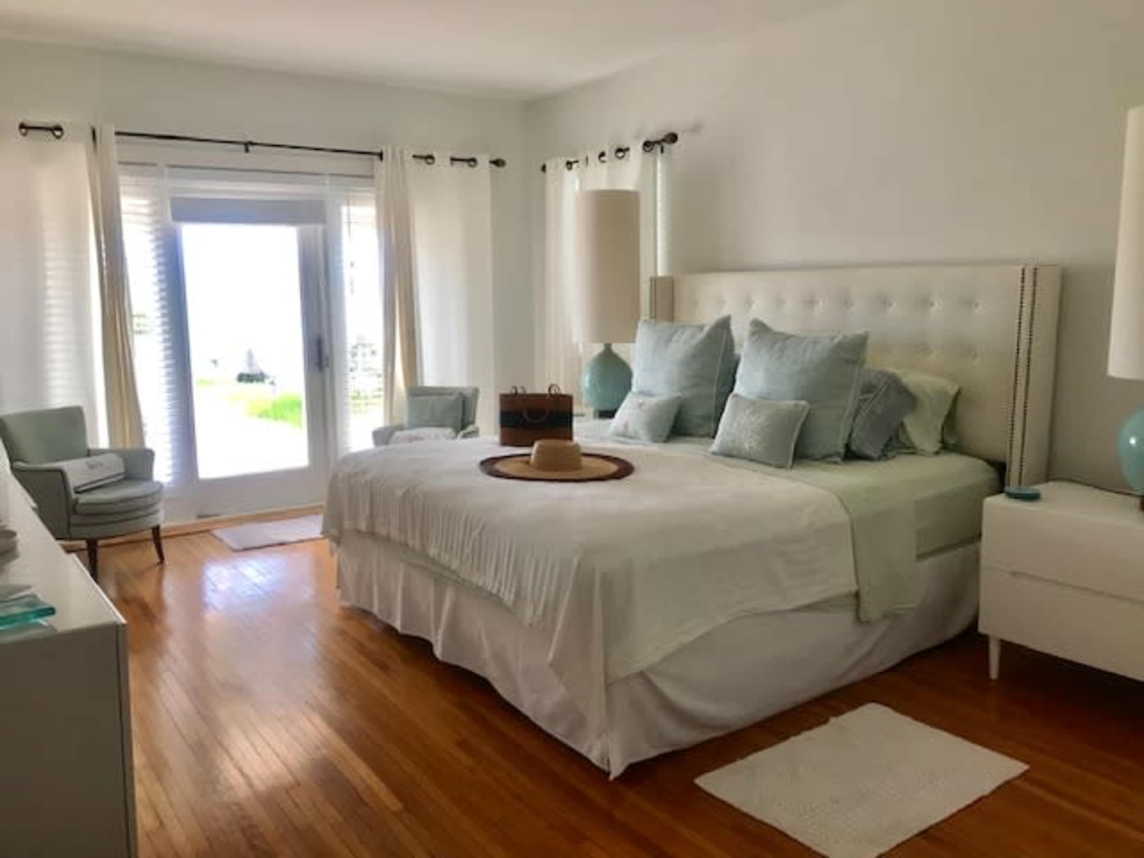 A neatly arranged bedroom with a large bed covered in light bedding, two bedside tables, and a view through glass doors leading to an outdoor space.