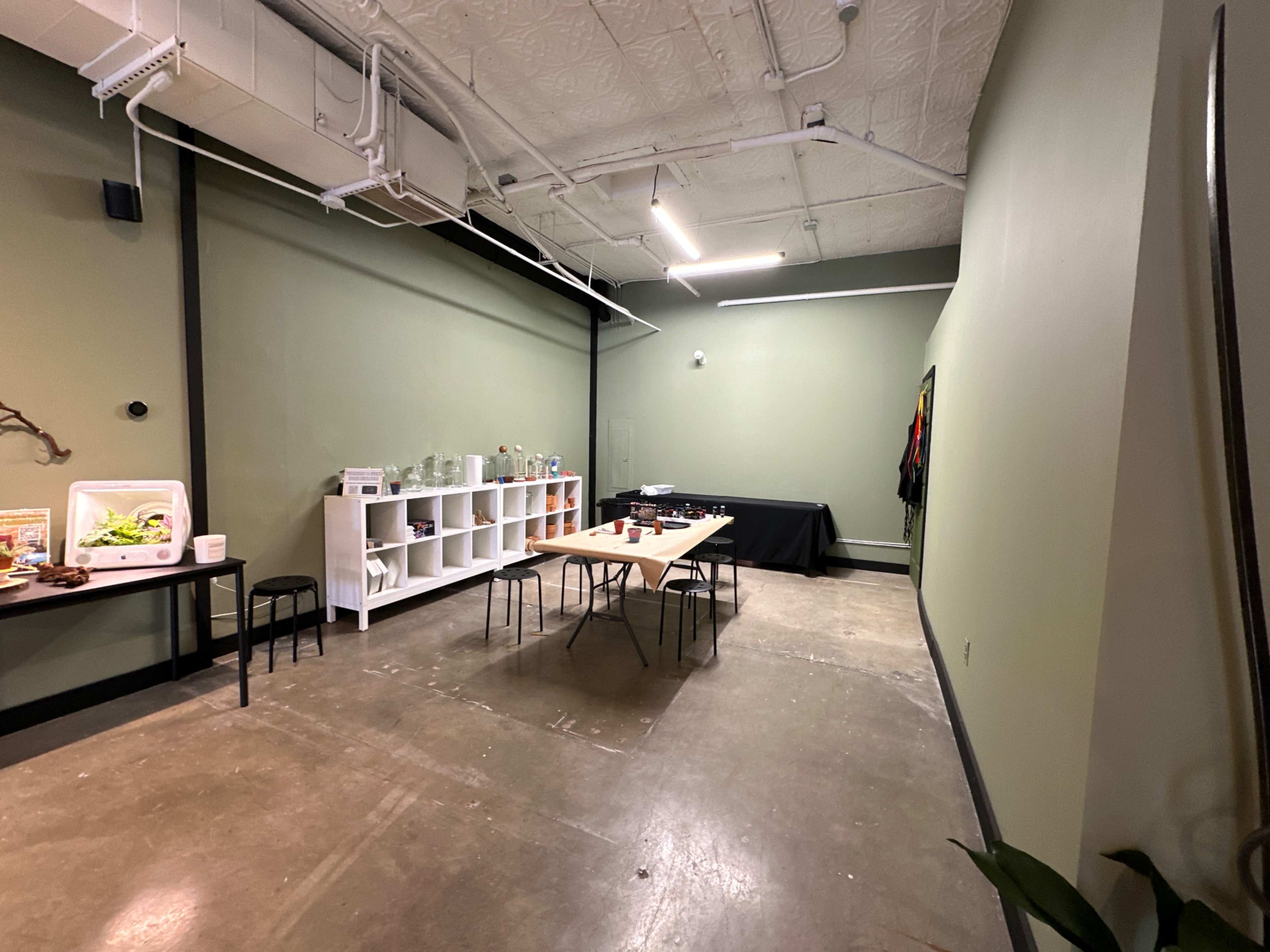 A sparse room with green walls, a polished concrete floor, and several tables set up along with shelving and a cooler.