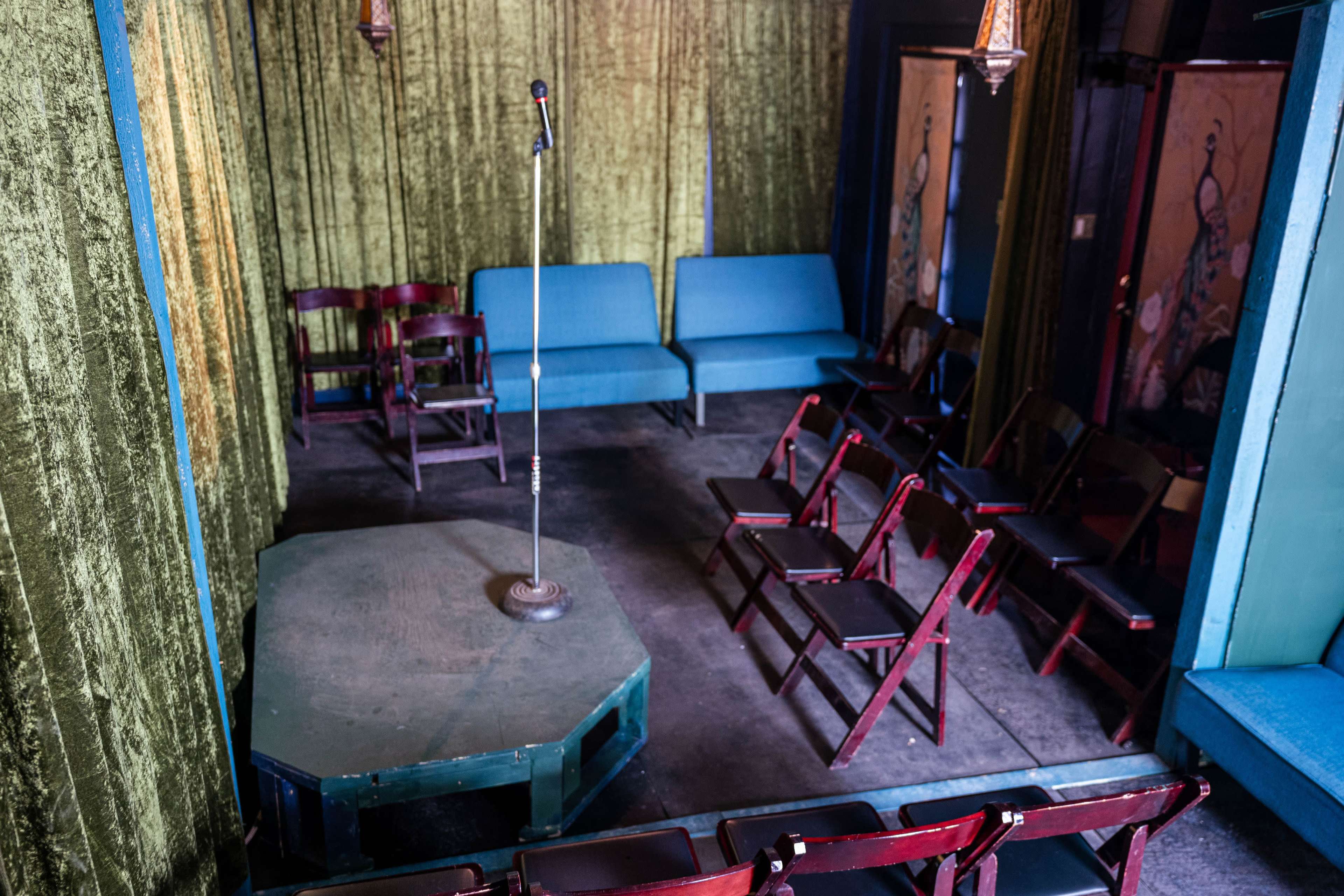 A small performance space with a microphone on a raised platform surrounded by chairs and blue couches.