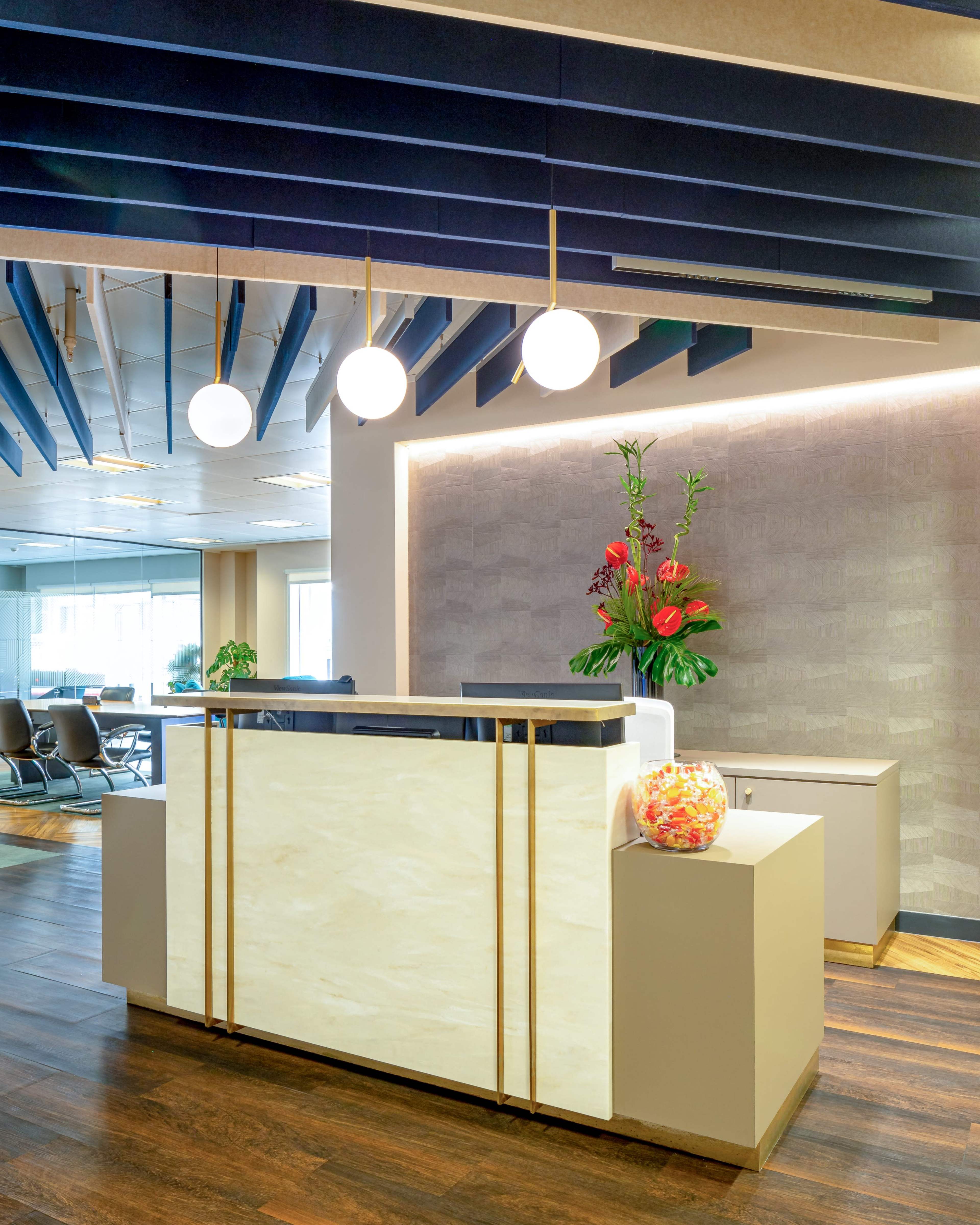 A modern reception area featuring a sleek front desk, pendant lights, and floral arrangements in a contemporary design.