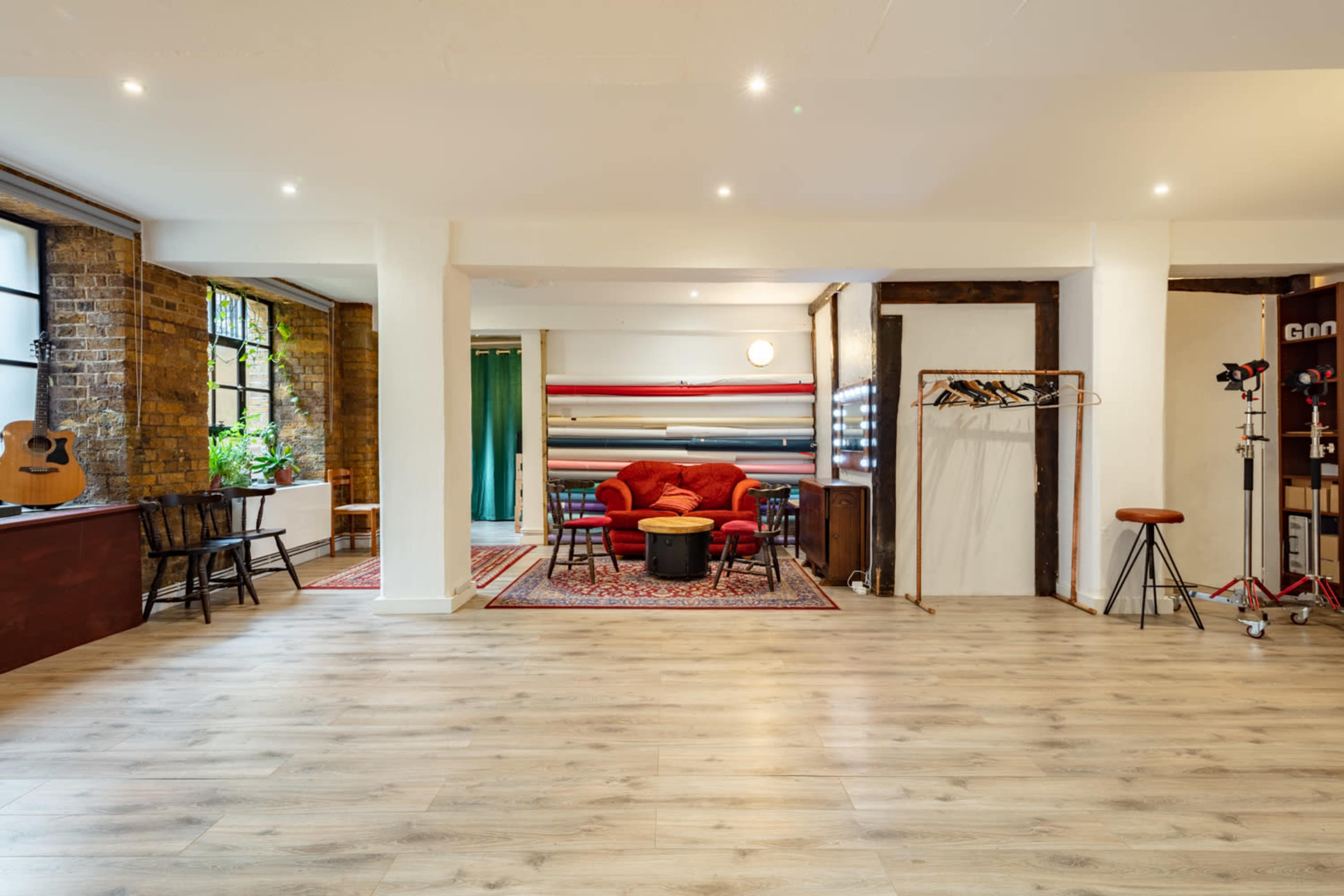 A spacious indoor area featuring a red sofa, a coffee table, and wooden flooring, with large windows and an acoustic guitar in one corner.
