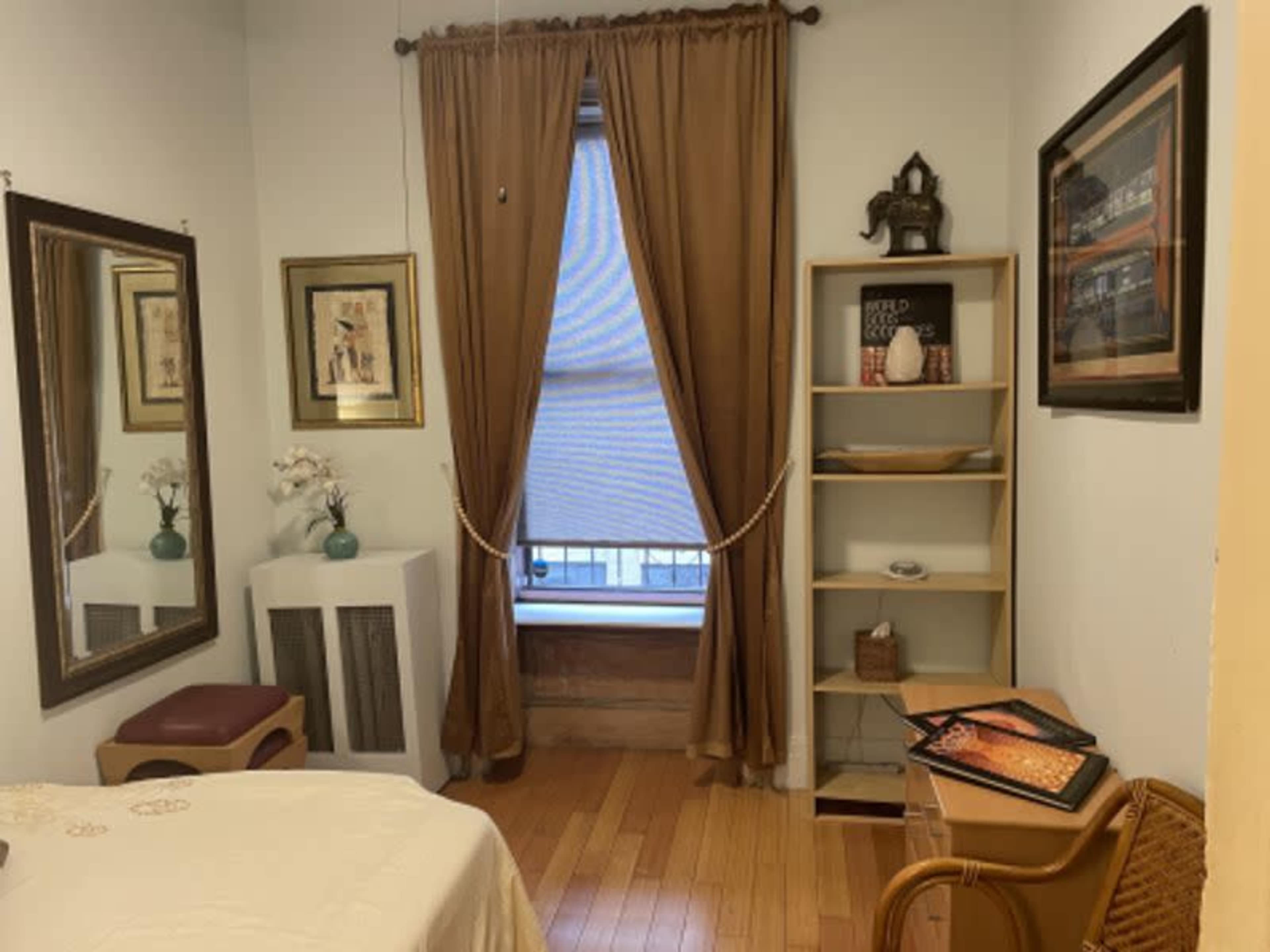The image shows a small room with a bed, a decorative mirror, a bookshelf, and a window covered by drapes.