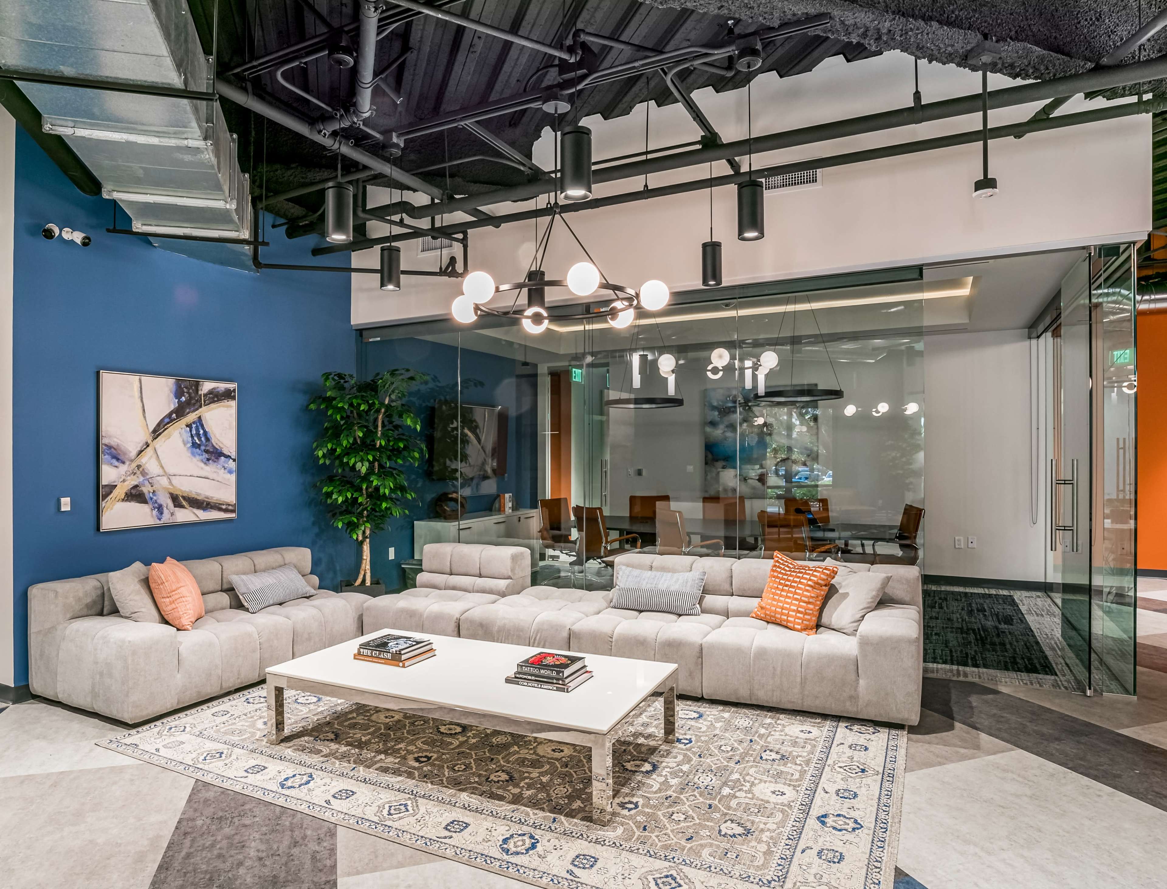 A modern lounge area features a large sofa, a coffee table, and a patterned rug beneath a suspended light fixture.