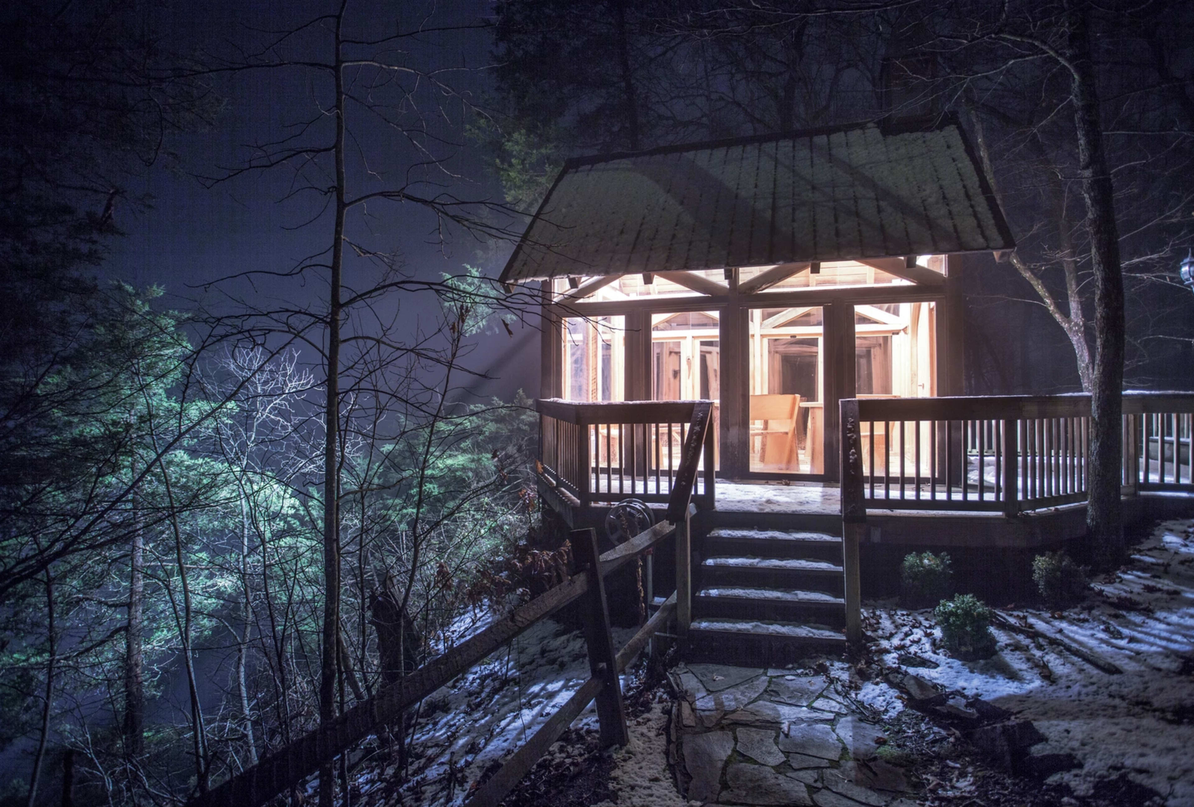 A wooden gazebo is illuminated at night, surrounded by trees and a stone pathway leading up to it.