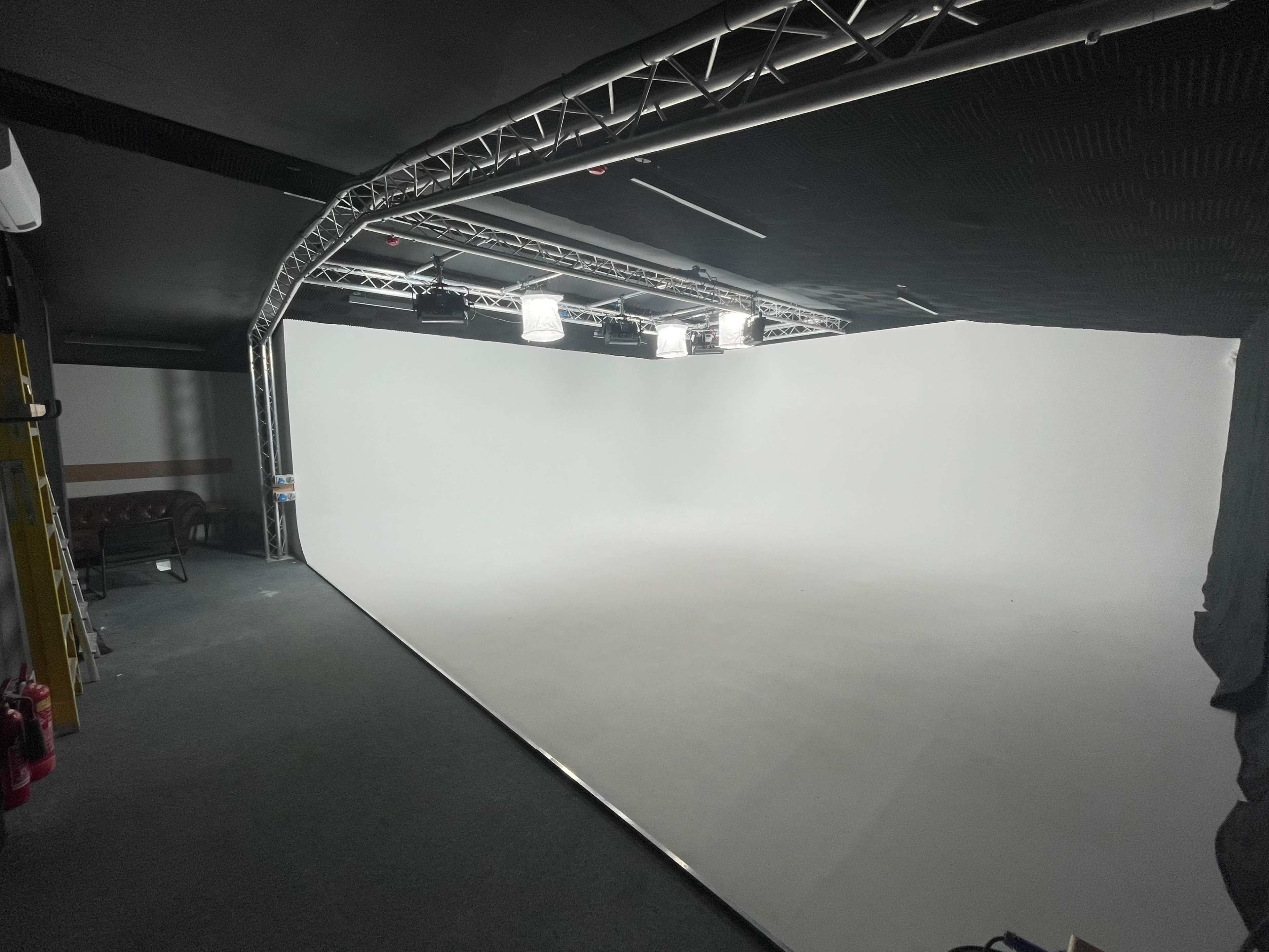 A minimalist studio space with a large white backdrop and overhead lighting.