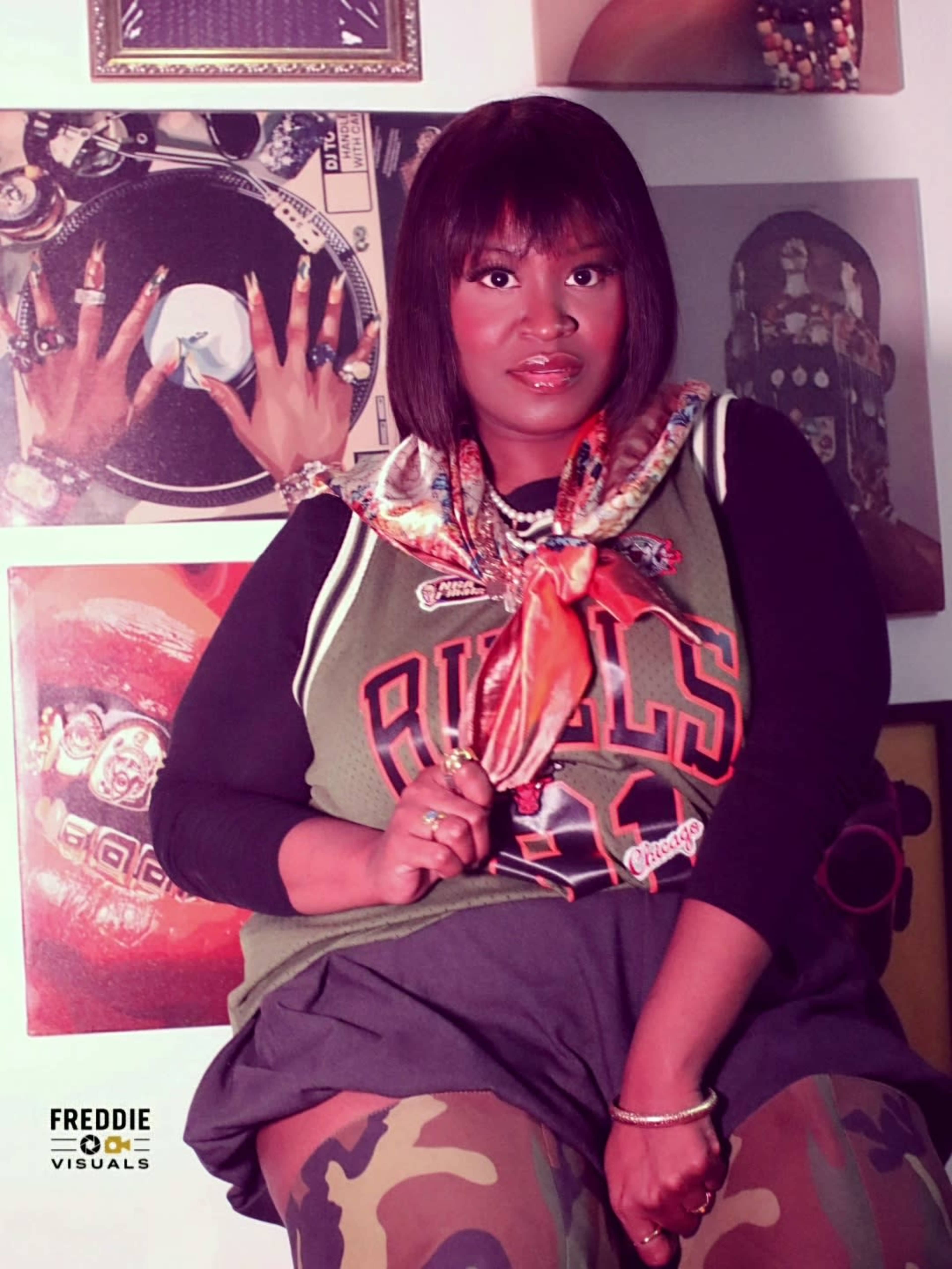 A woman poses in front of a wall adorned with various photographs, wearing a sports jersey and holding a scarf.