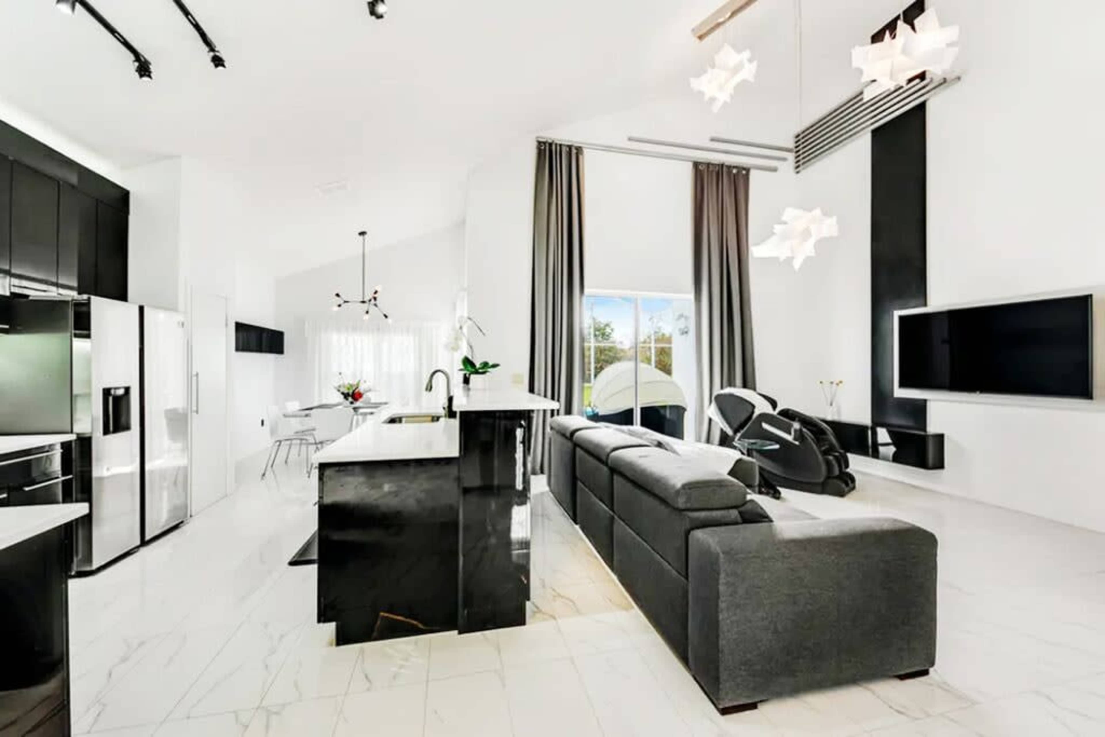 A modern open-plan kitchen and living area featuring sleek black cabinetry, a large gray sofa, and ample natural light from a window.