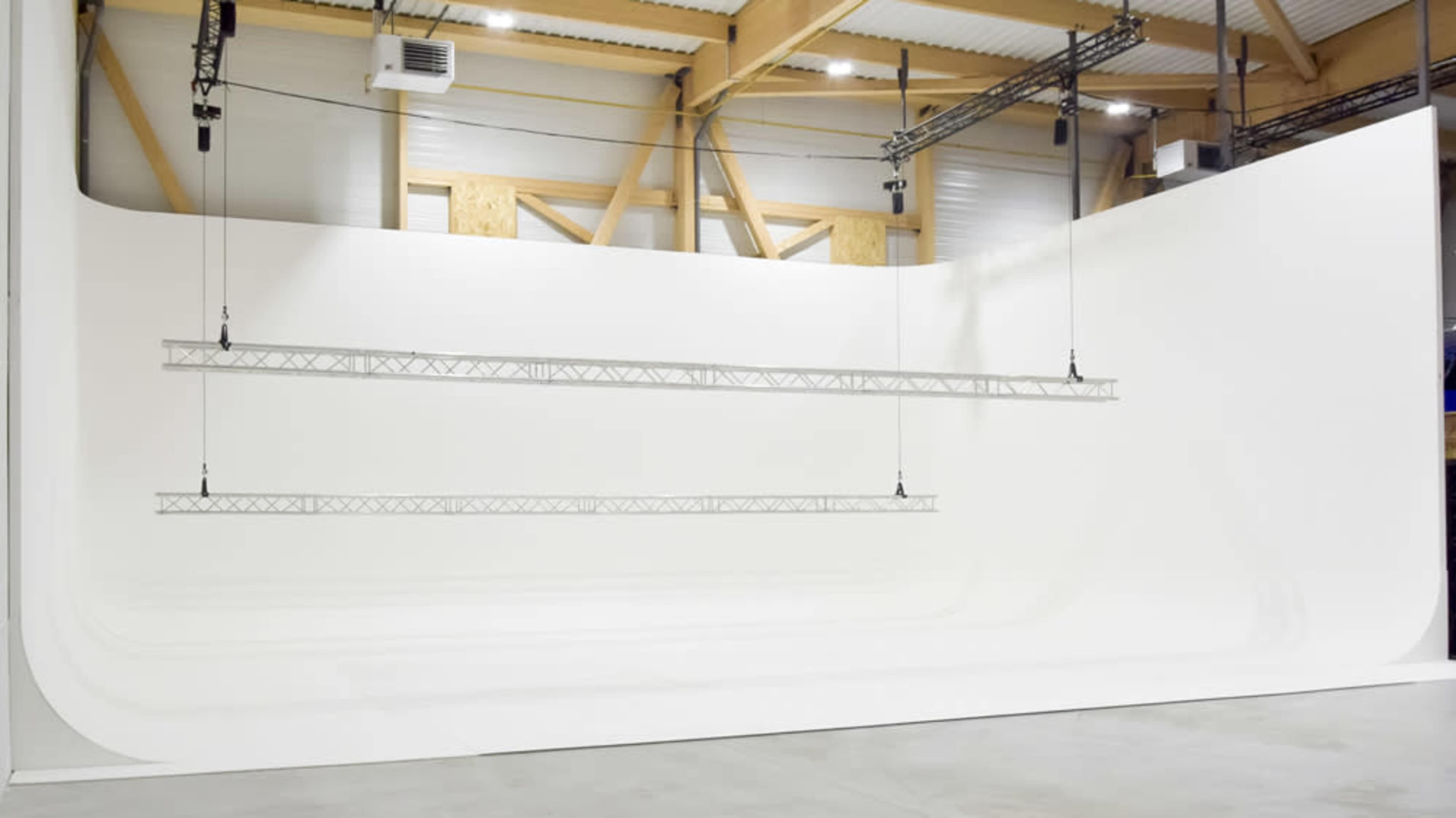 The image shows a spacious white studio with a curved backdrop and hanging truss systems for lighting.