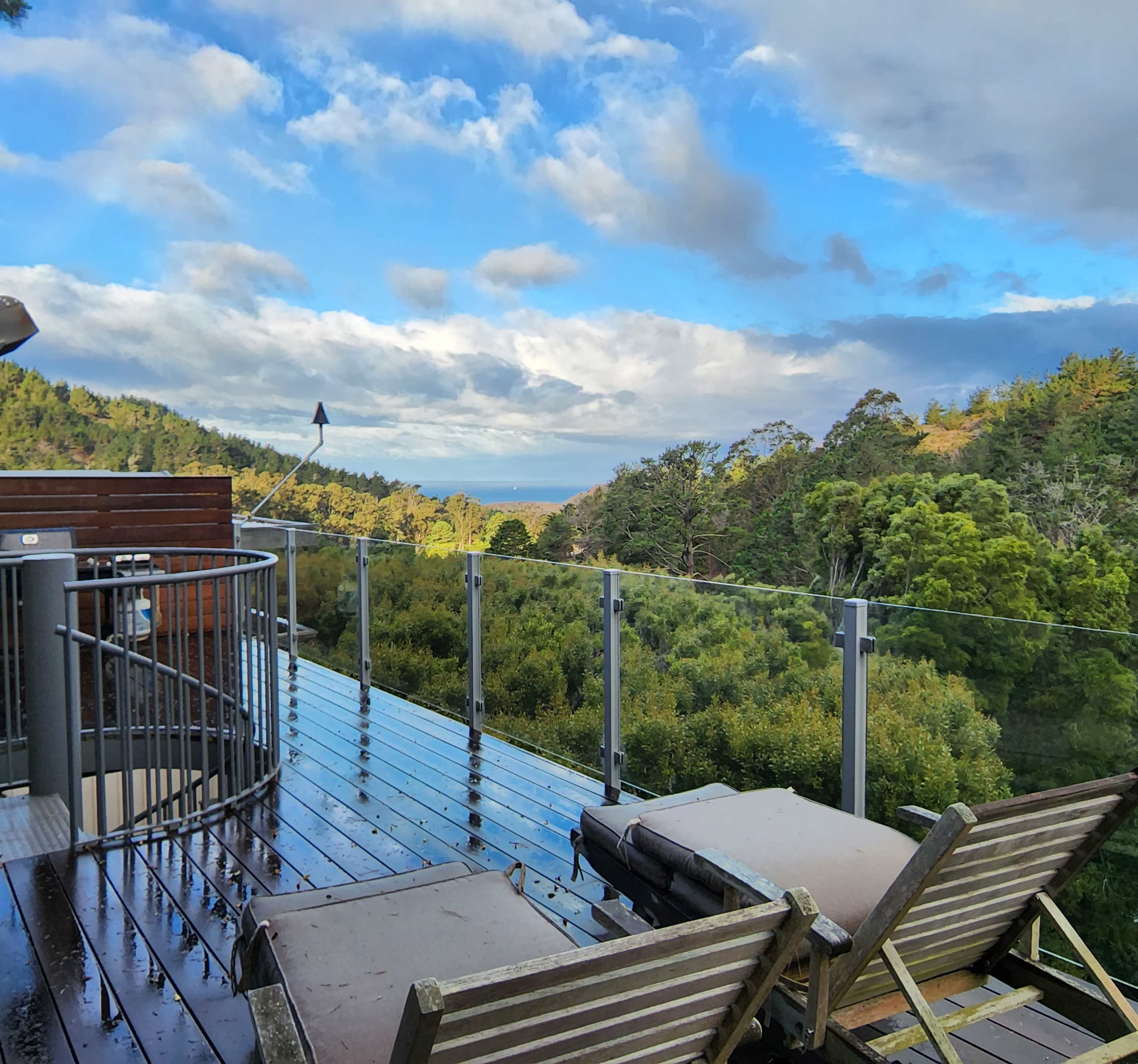 A deck with wooden loungers overlooks a lush green landscape and a cloudy sky.