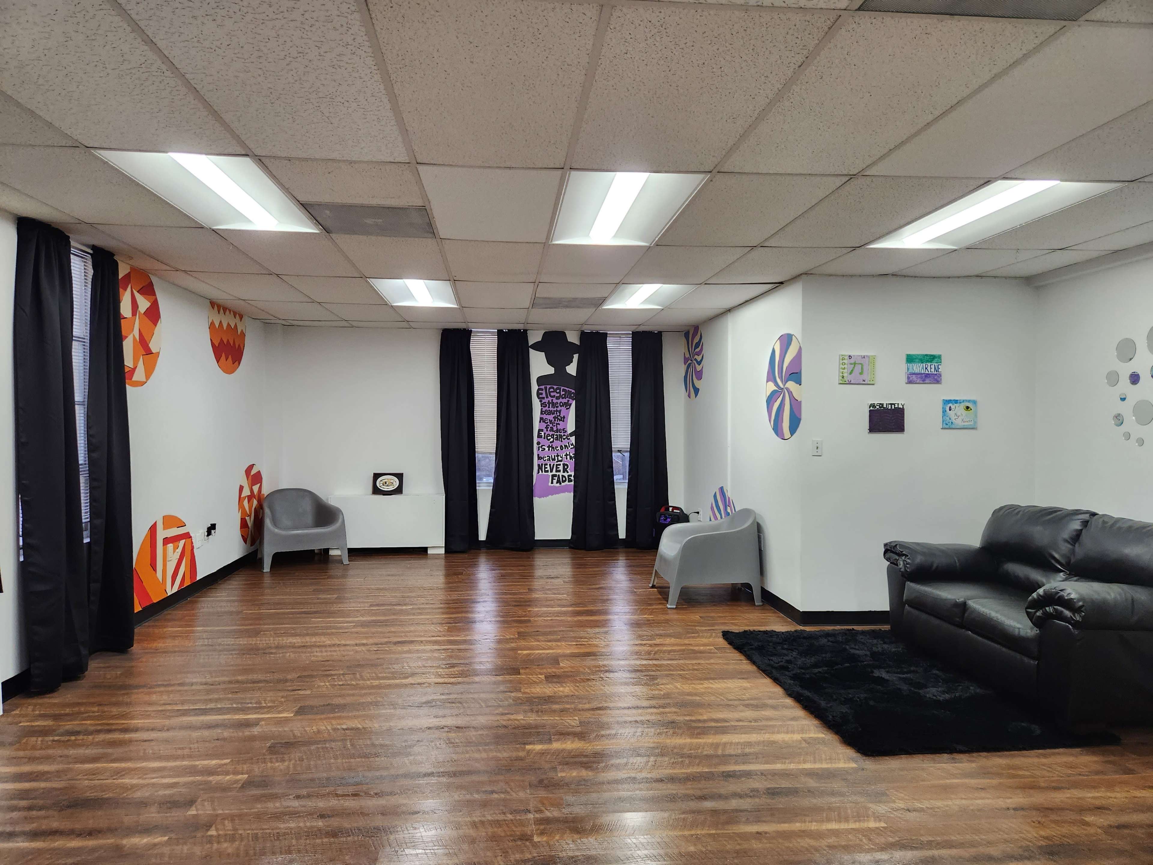 A spacious interior features dark furniture, colorful wall art, and large windows with black curtains.