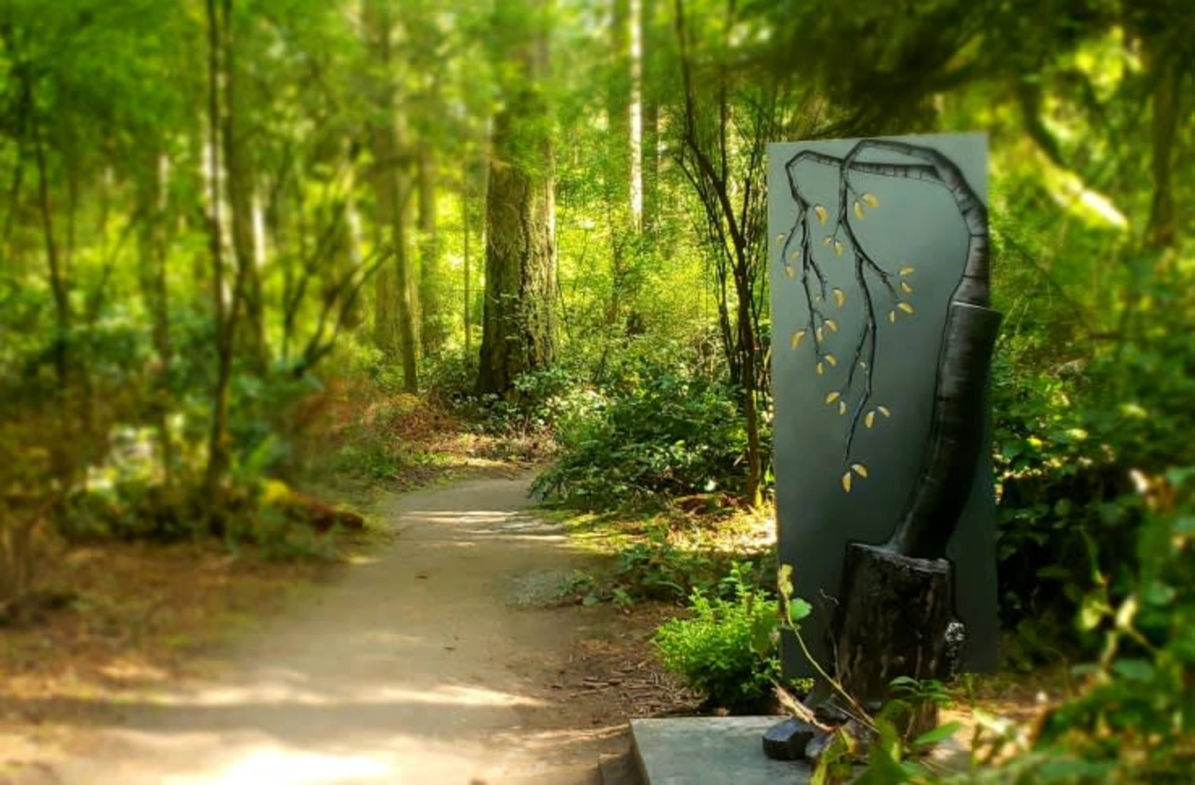 A walking path leads into a lush forest, with a large abstract art piece resembling a tree trunk and branches positioned nearby.
