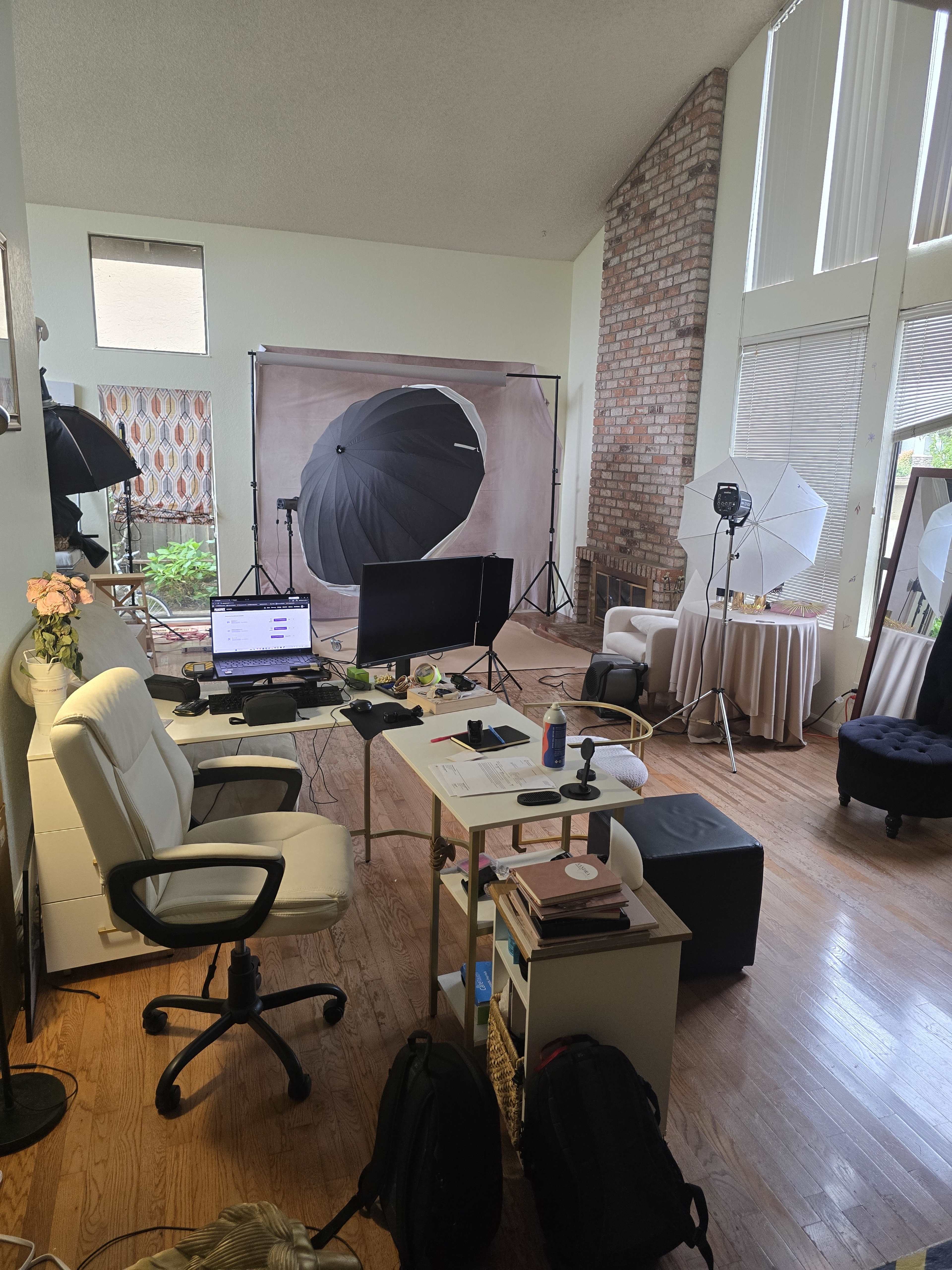 The image shows a photography studio with various lighting setups, a desk with a computer and accessories, and multiple backdrops arranged in a spacious room.