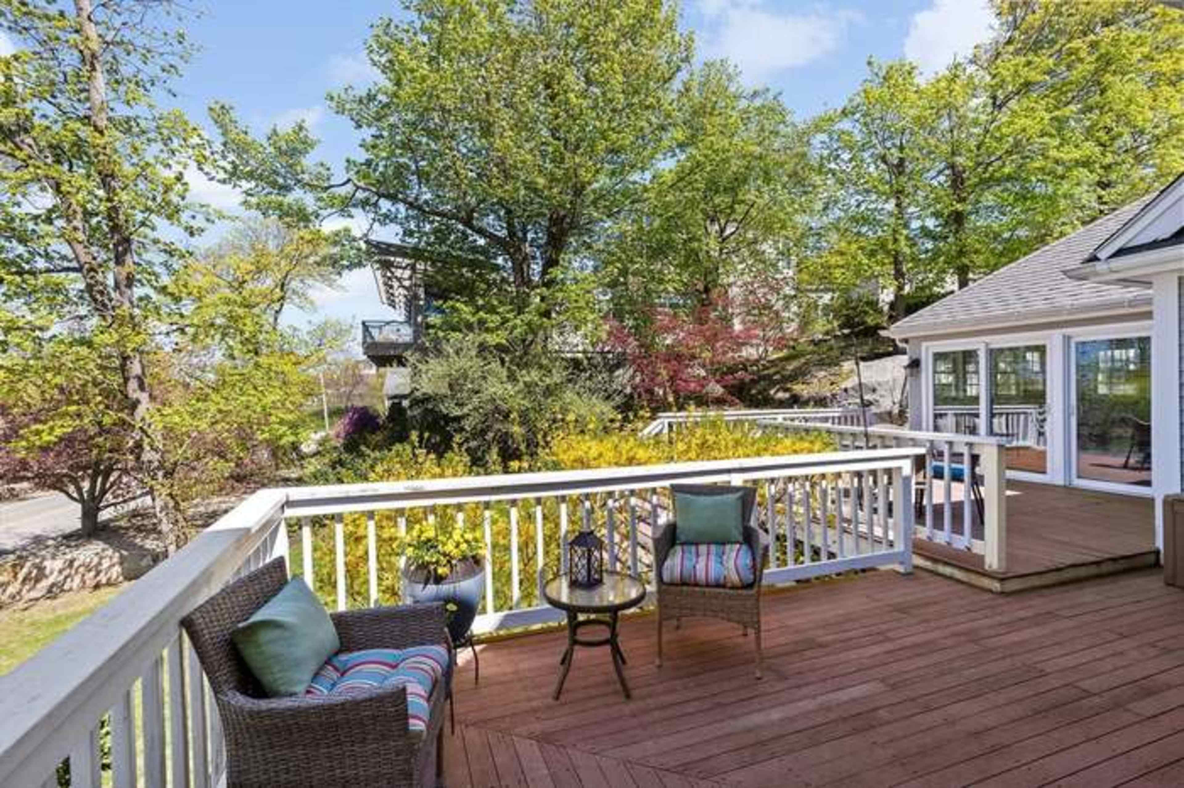 The image shows a wooden deck with two chairs and a small table, surrounded by trees and greenery.