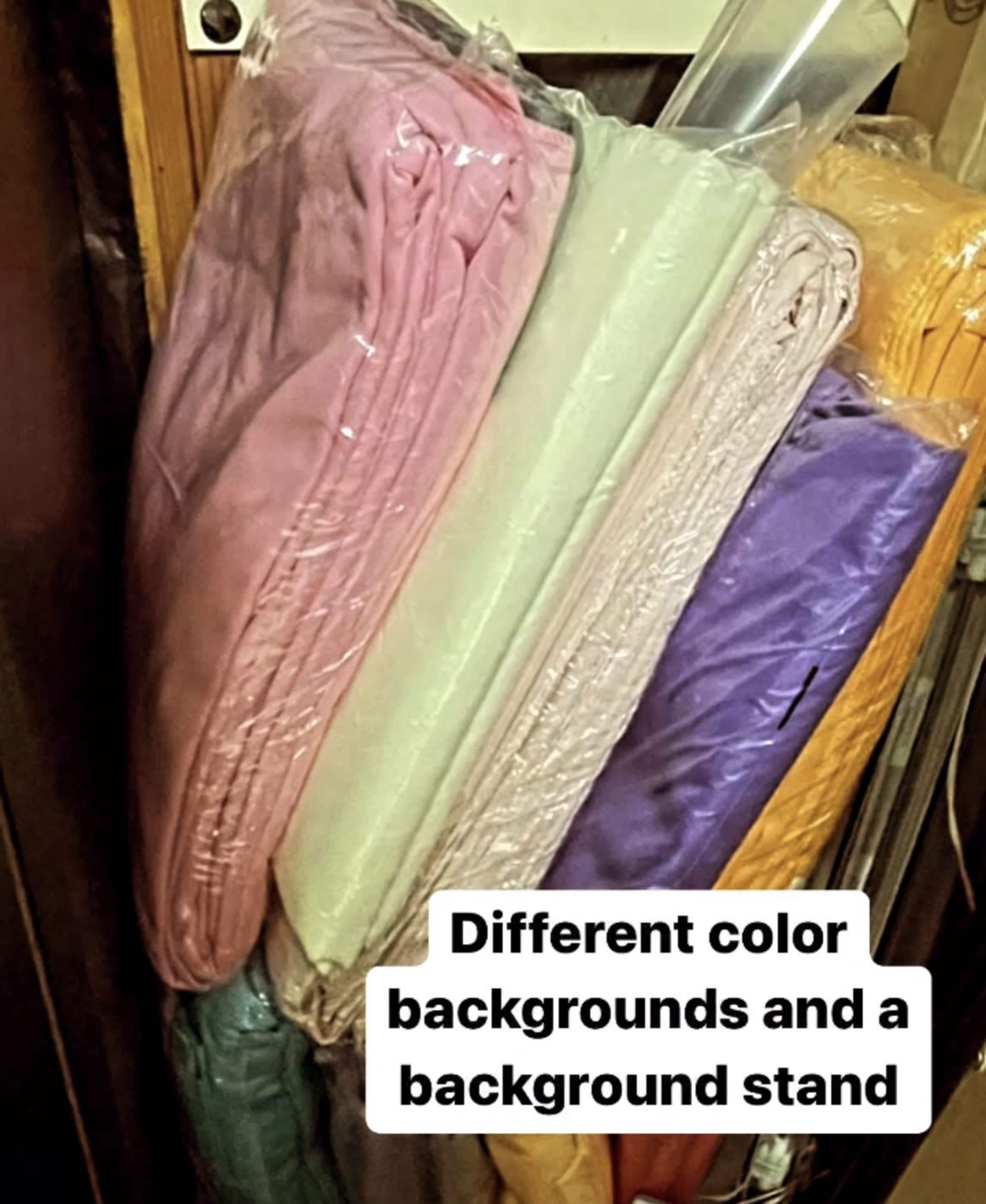Several folded fabric backgrounds in various colors stacked next to a background stand.