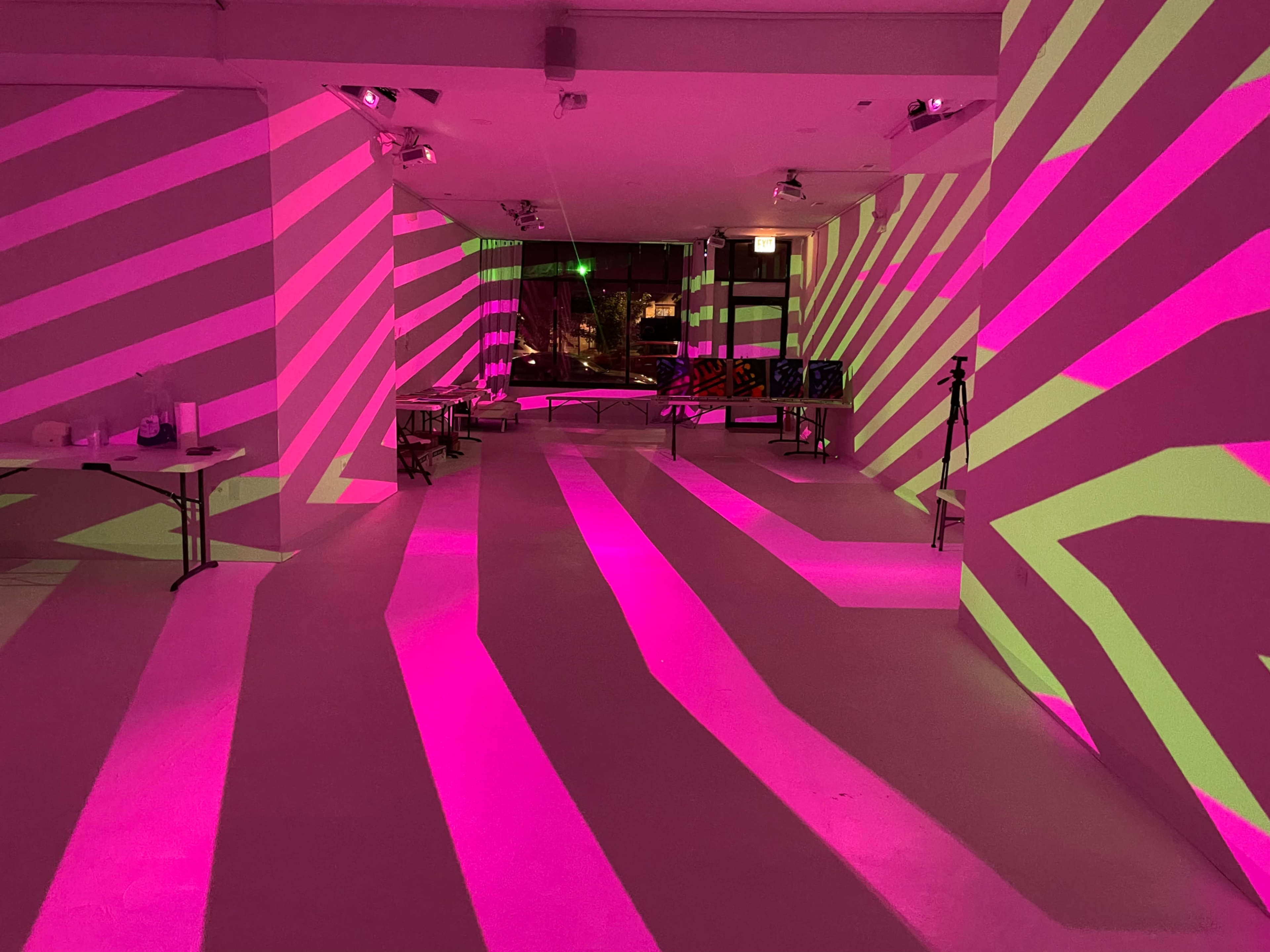 A room with pink and white striped projections illuminating the walls and floor, creating a dynamic visual effect.