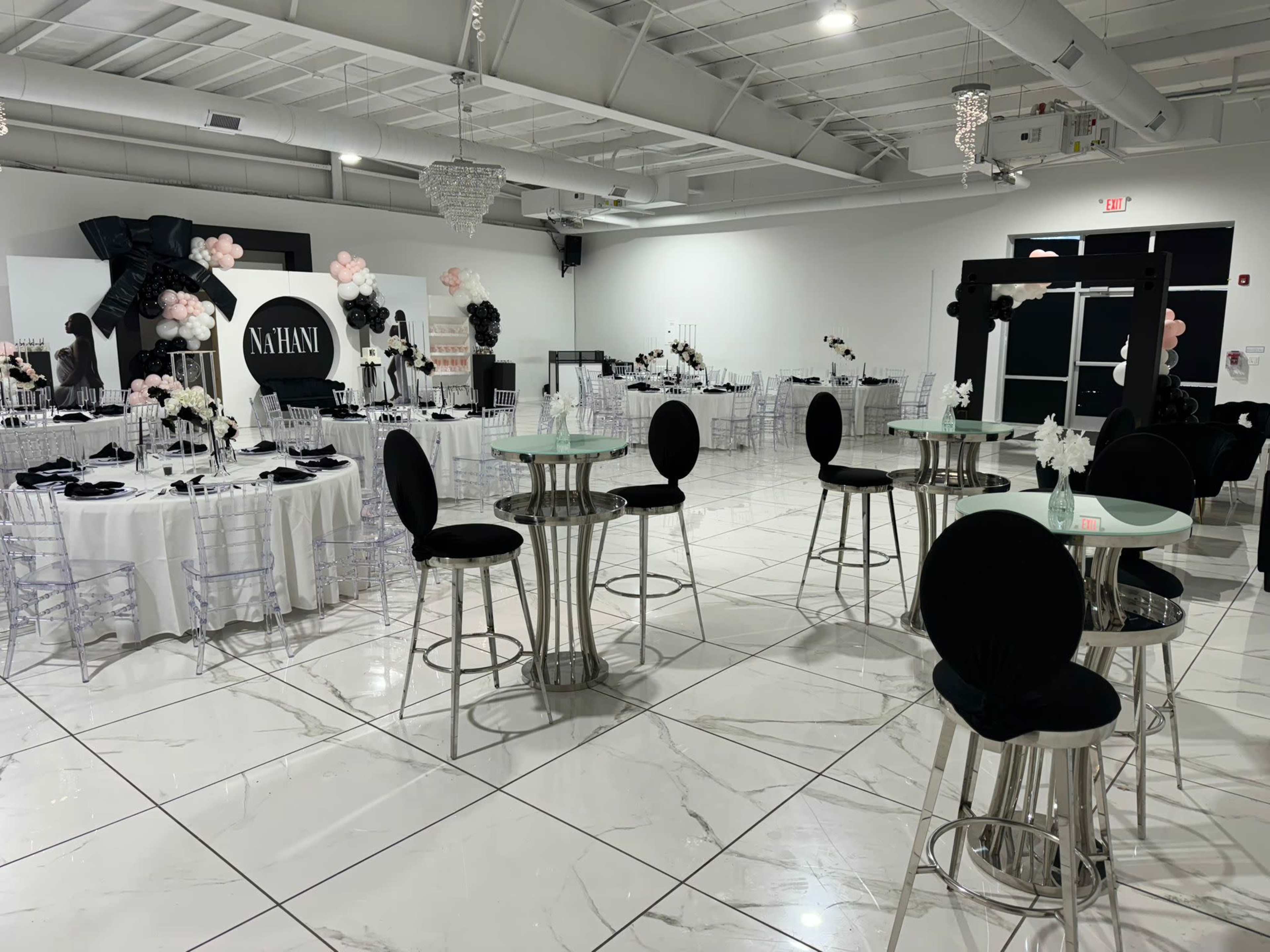 The image shows a formal event space with elegantly arranged tables, black and white decorations, and a chandelier.