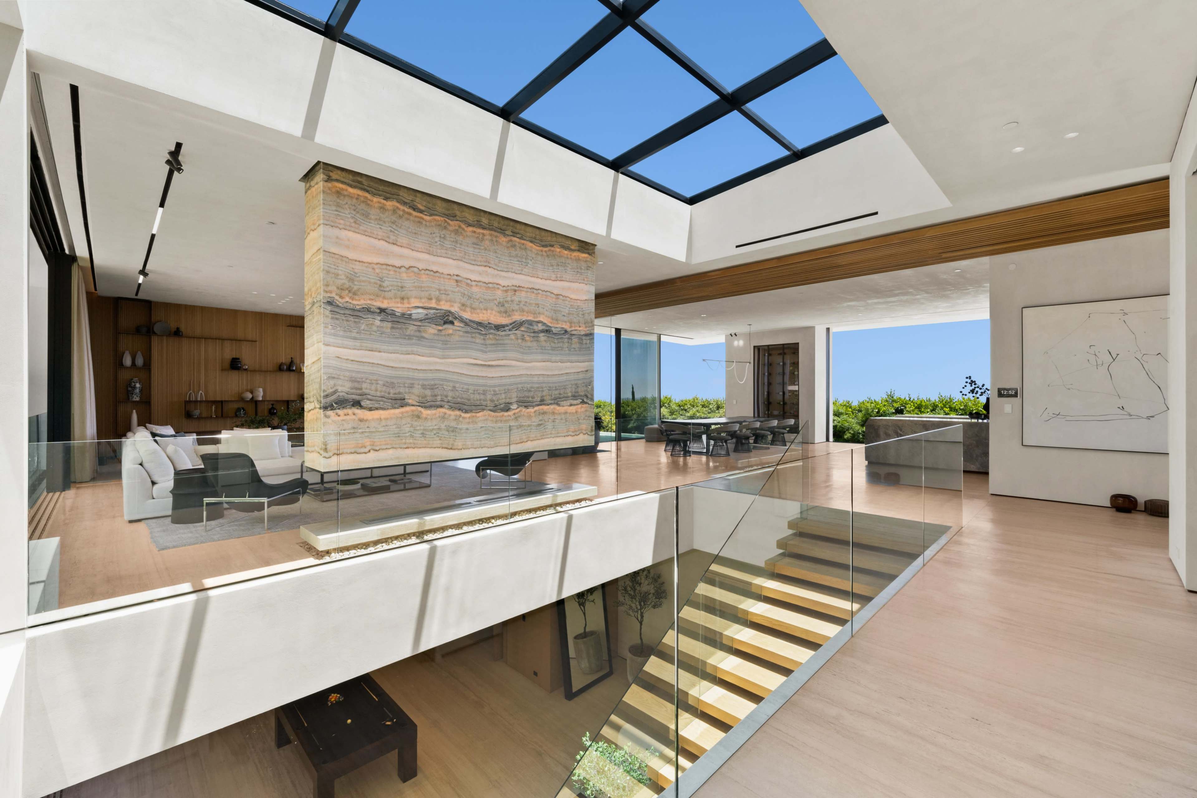 A modern, open-concept living space featuring a large stone partition, glass railings, and ample natural light from a skylight.