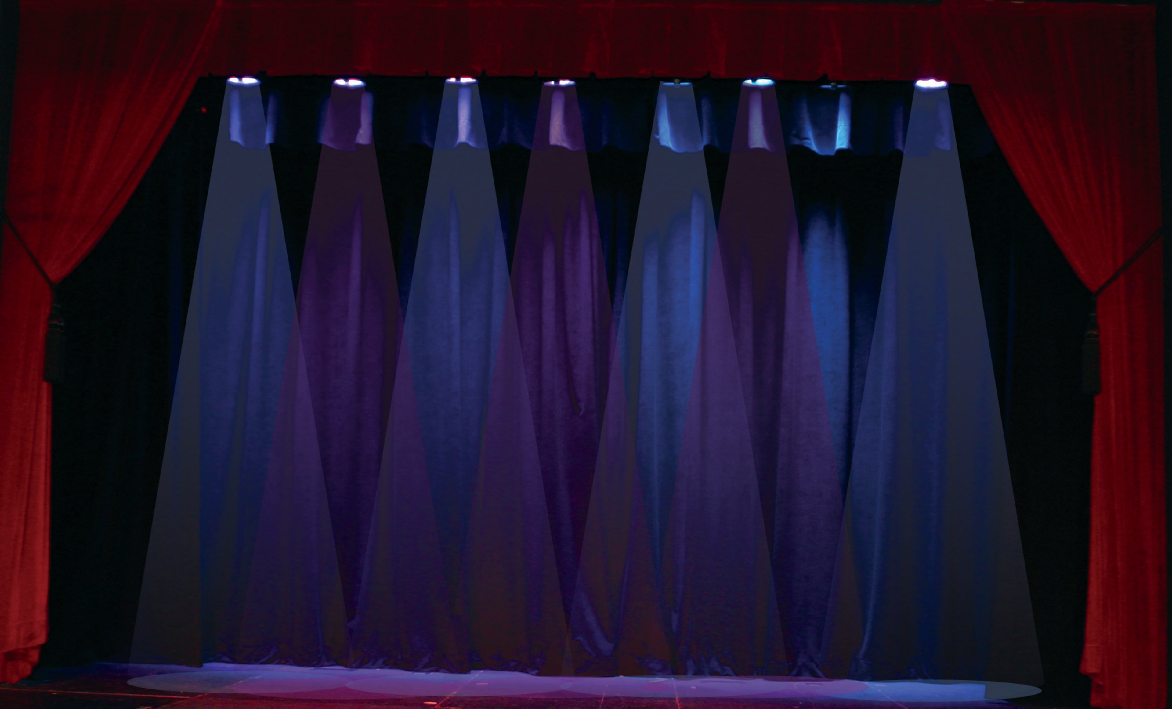 The image shows an empty stage with dark curtains and blue and purple lighting.