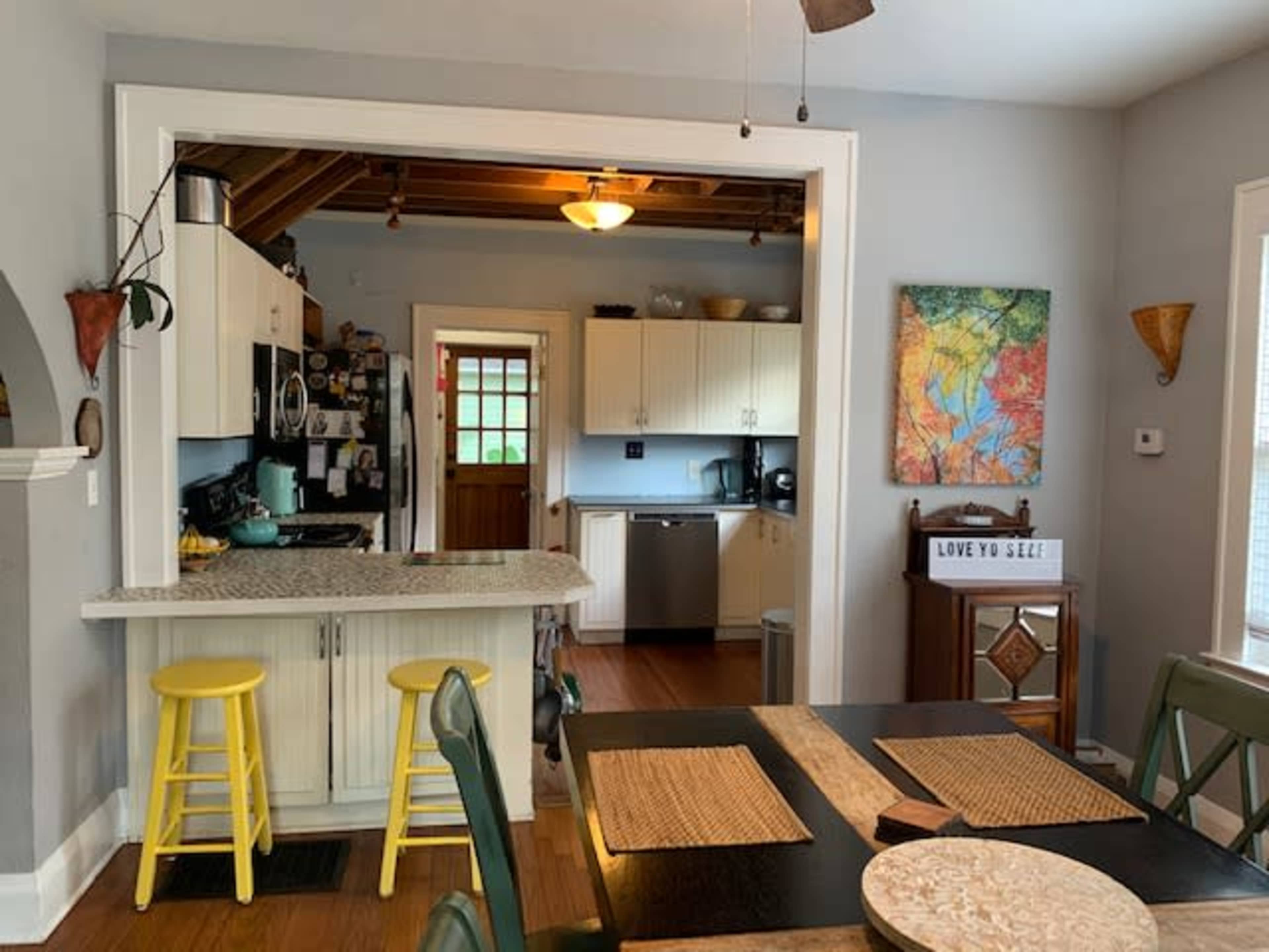 A bright kitchen area with white cabinets, a gray wall, and a dining table set near a window.