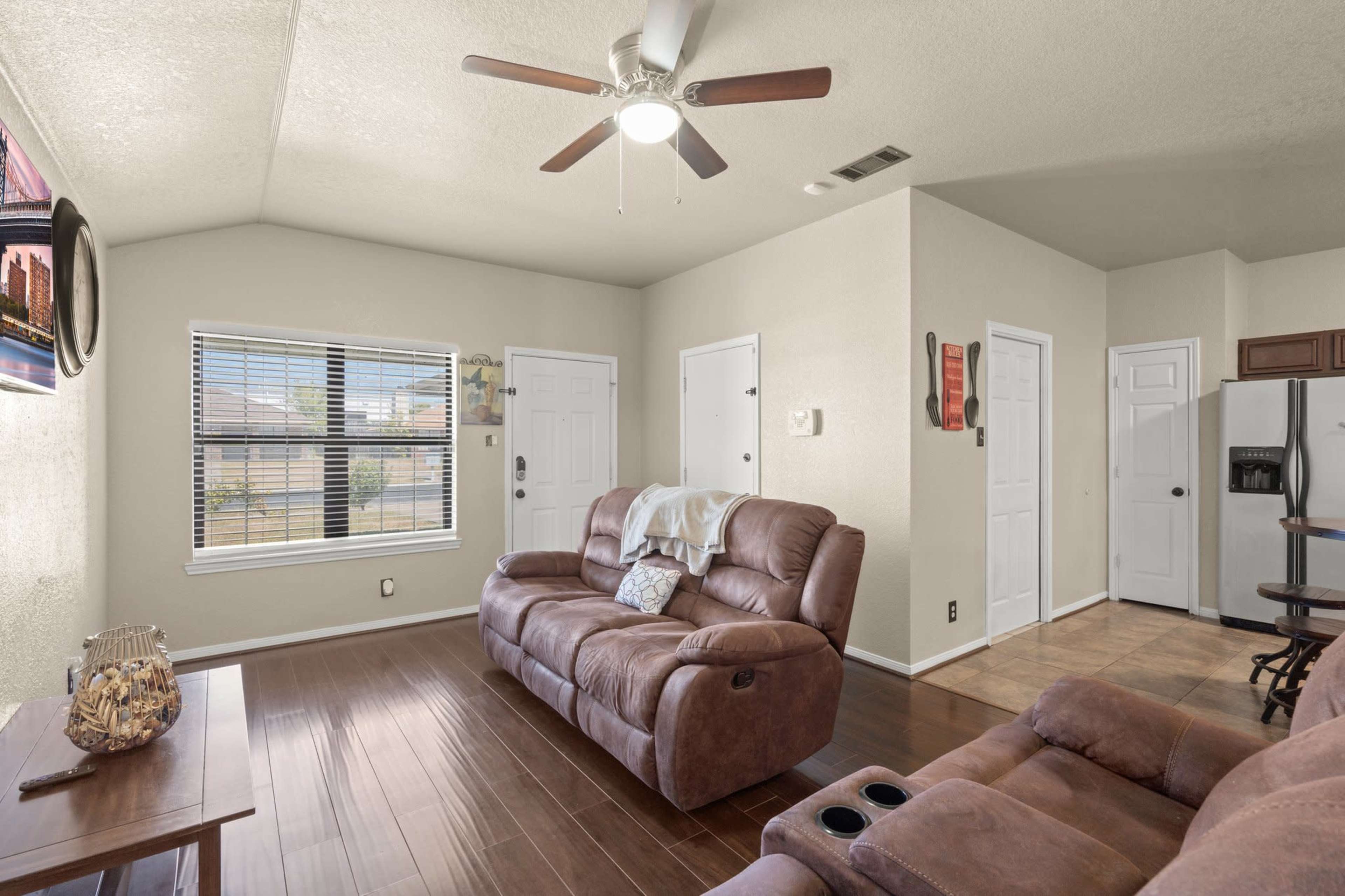 A living room with two brown recliners facing a television and a window, featuring wooden flooring and adjoining kitchen and entryway areas.