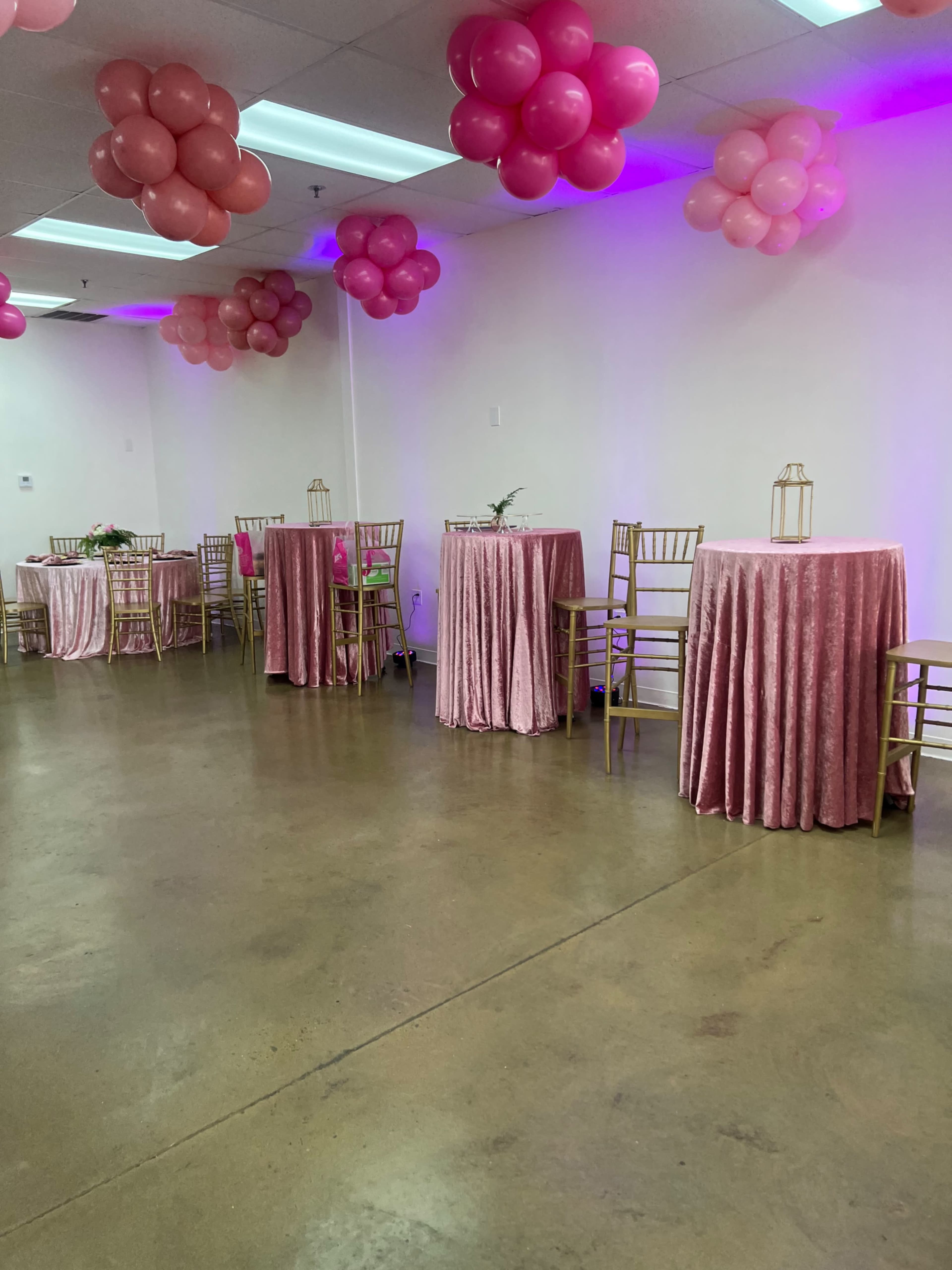 A room decorated with pink balloons and tables covered in pink tablecloths, set up for an event.