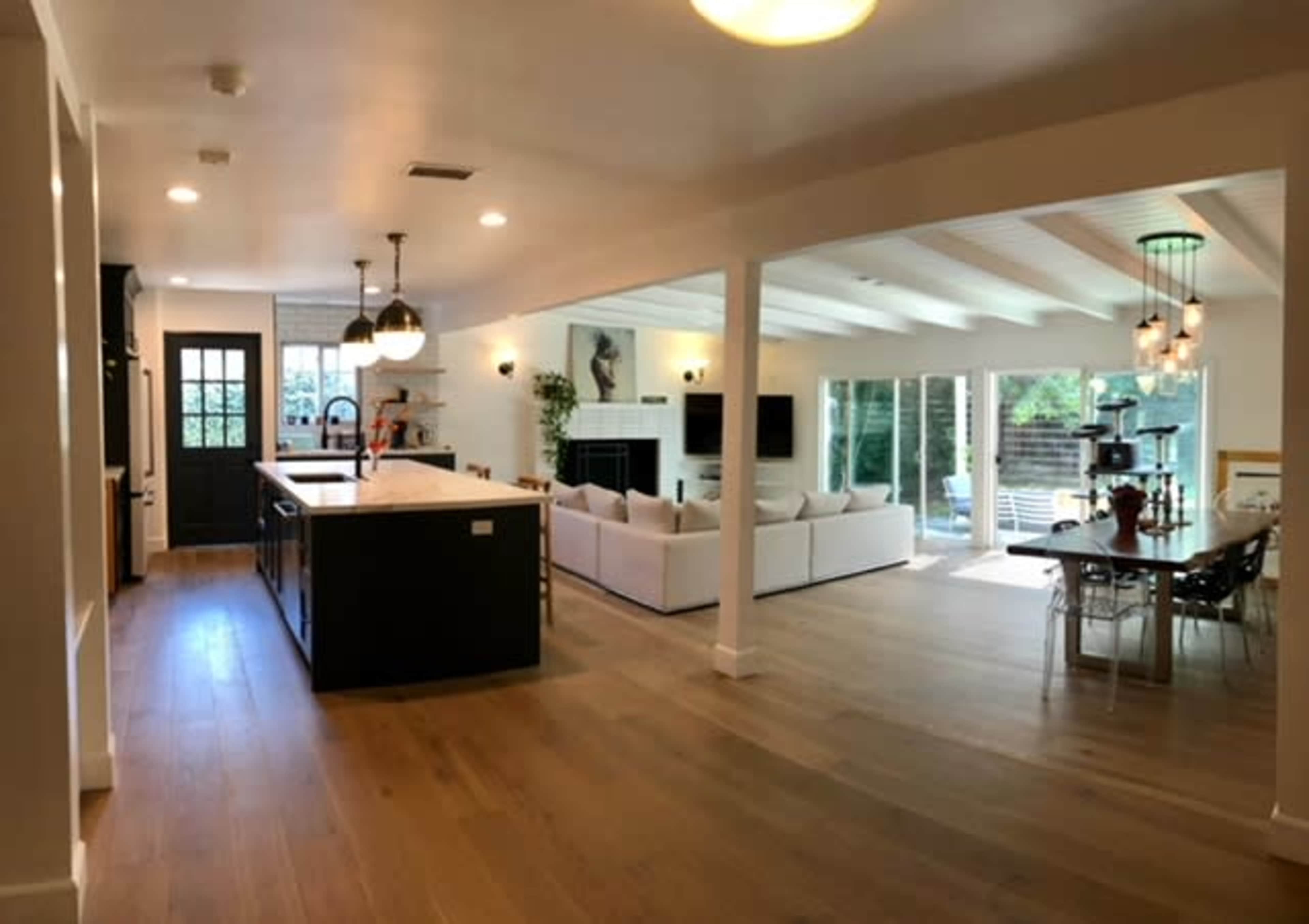 The image shows an open-concept living space featuring a kitchen with an island, a seating area with a large couch, and a dining area with a table.