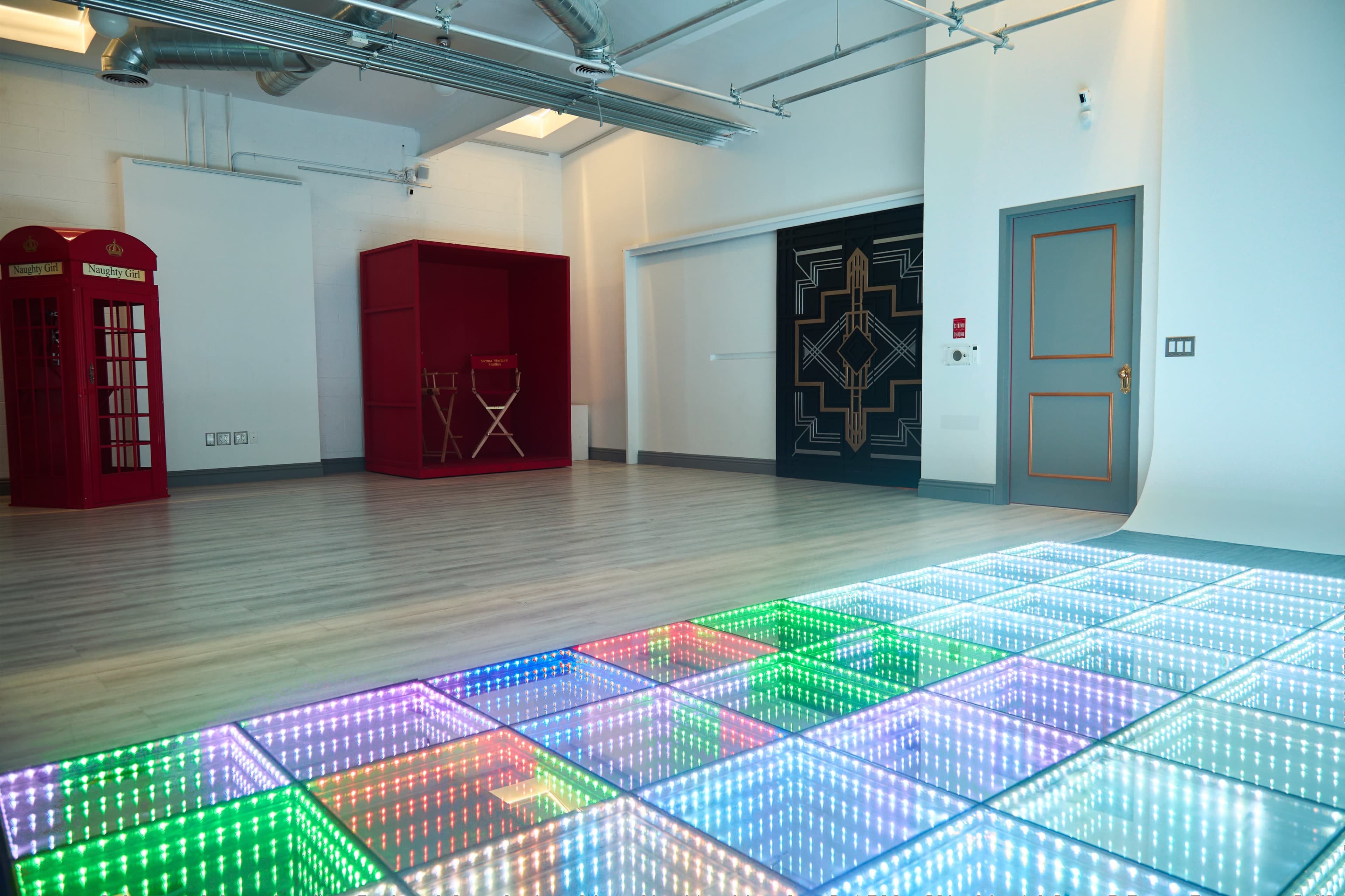 The image shows a modern room with a colorful LED dance floor, red seating area, and geometric wall art.