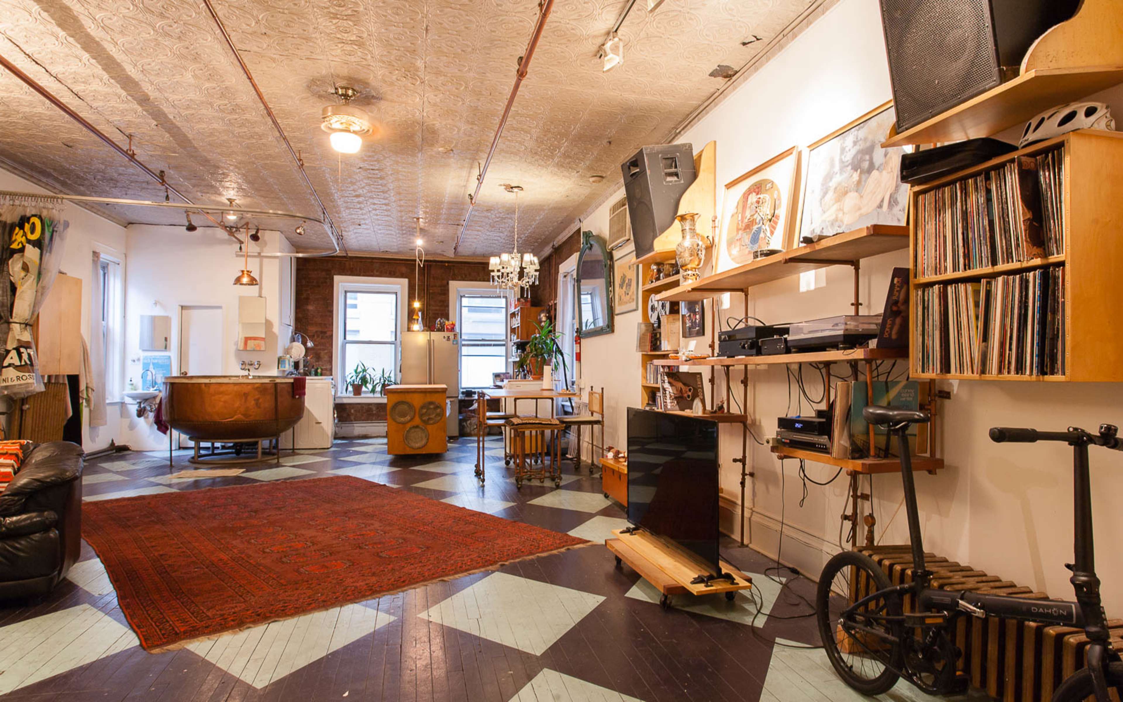 A spacious, eclectic room featuring a wooden bathtub, a record player with vinyl records, and patterned flooring.