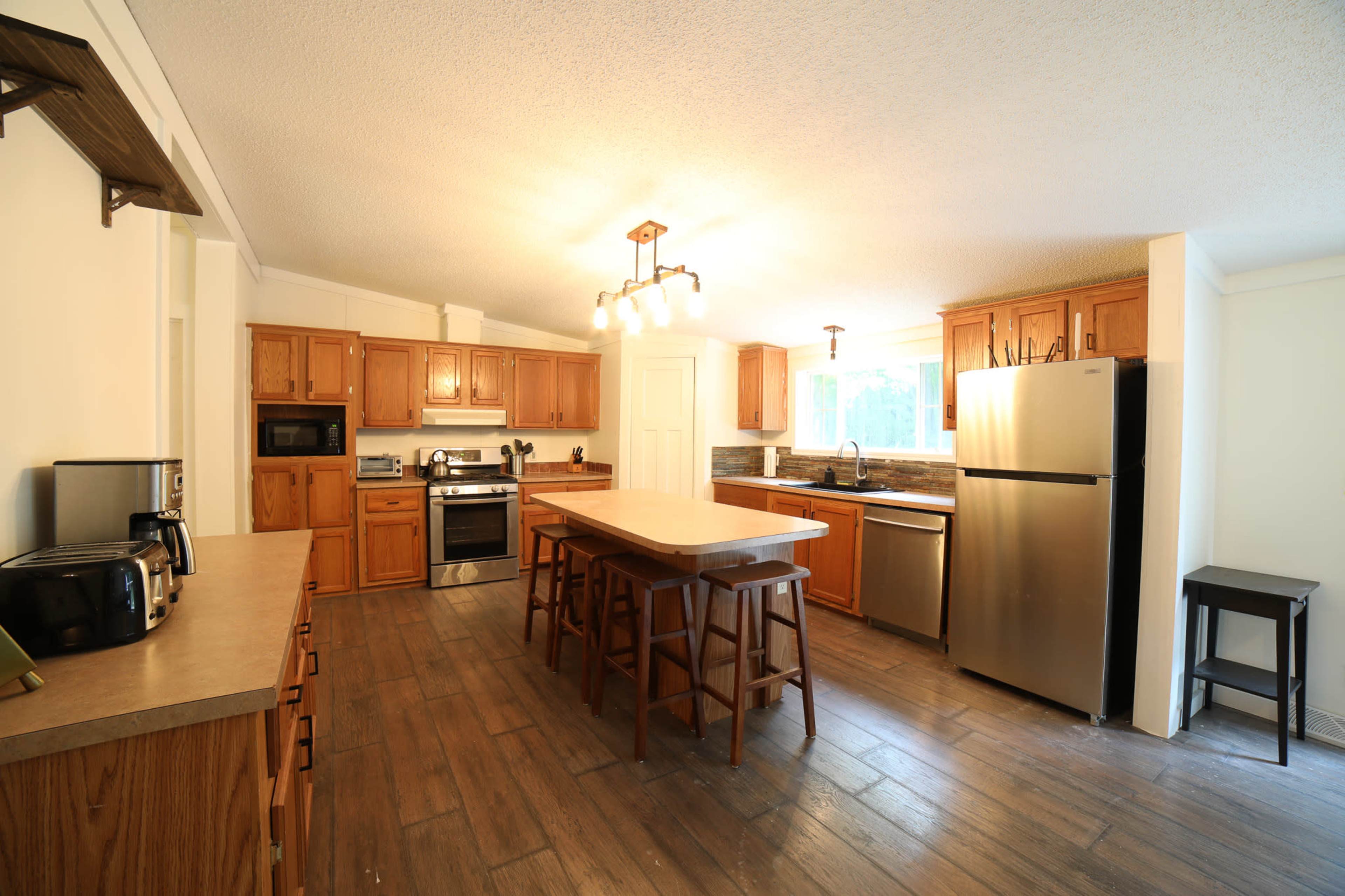 A spacious kitchen featuring wooden cabinets, stainless steel appliances, and an island with bar stools.