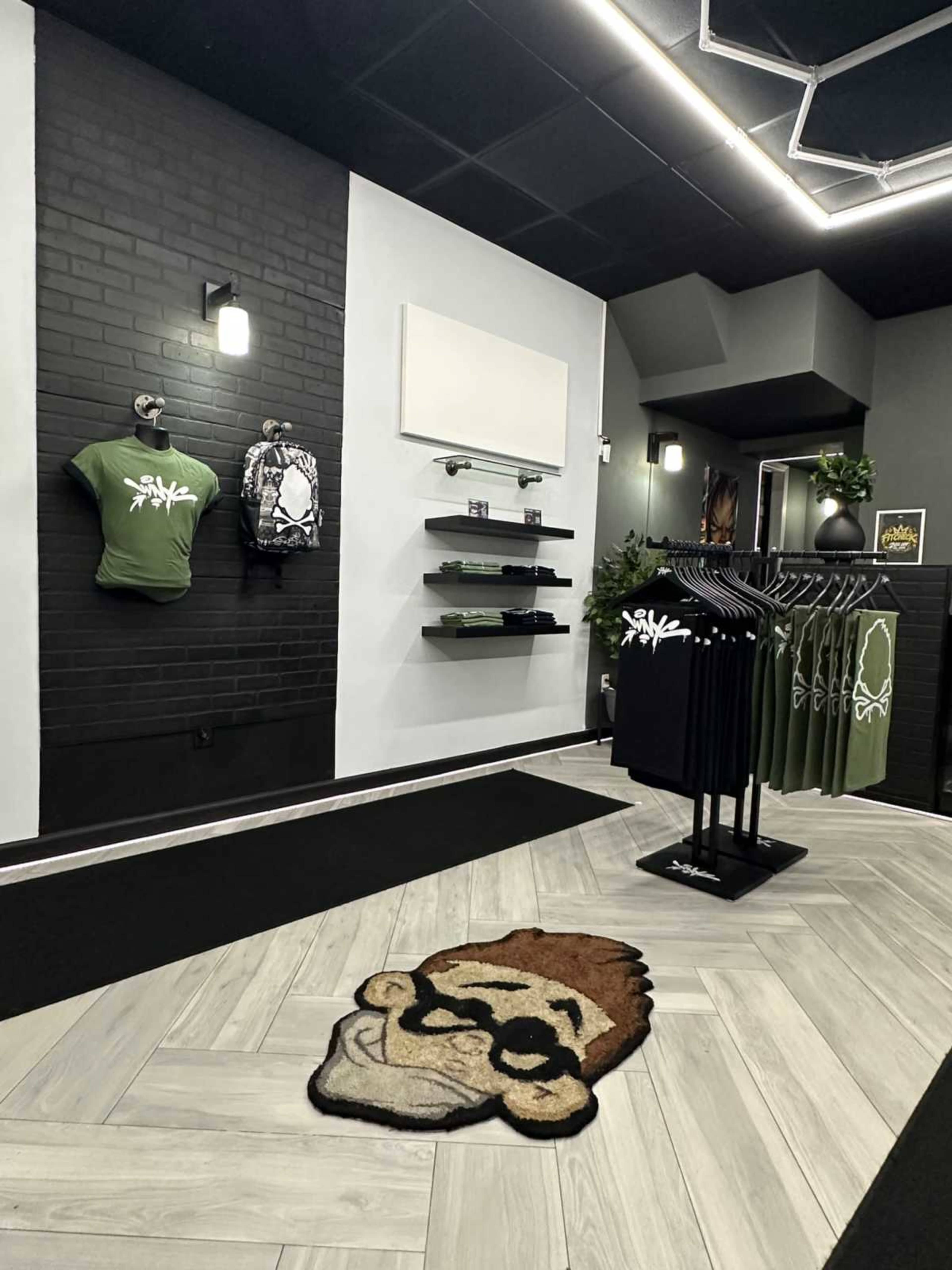 The image shows a retail store interior featuring green t-shirts on display, black clothing racks, and a cartoon monkey rug on the floor.
