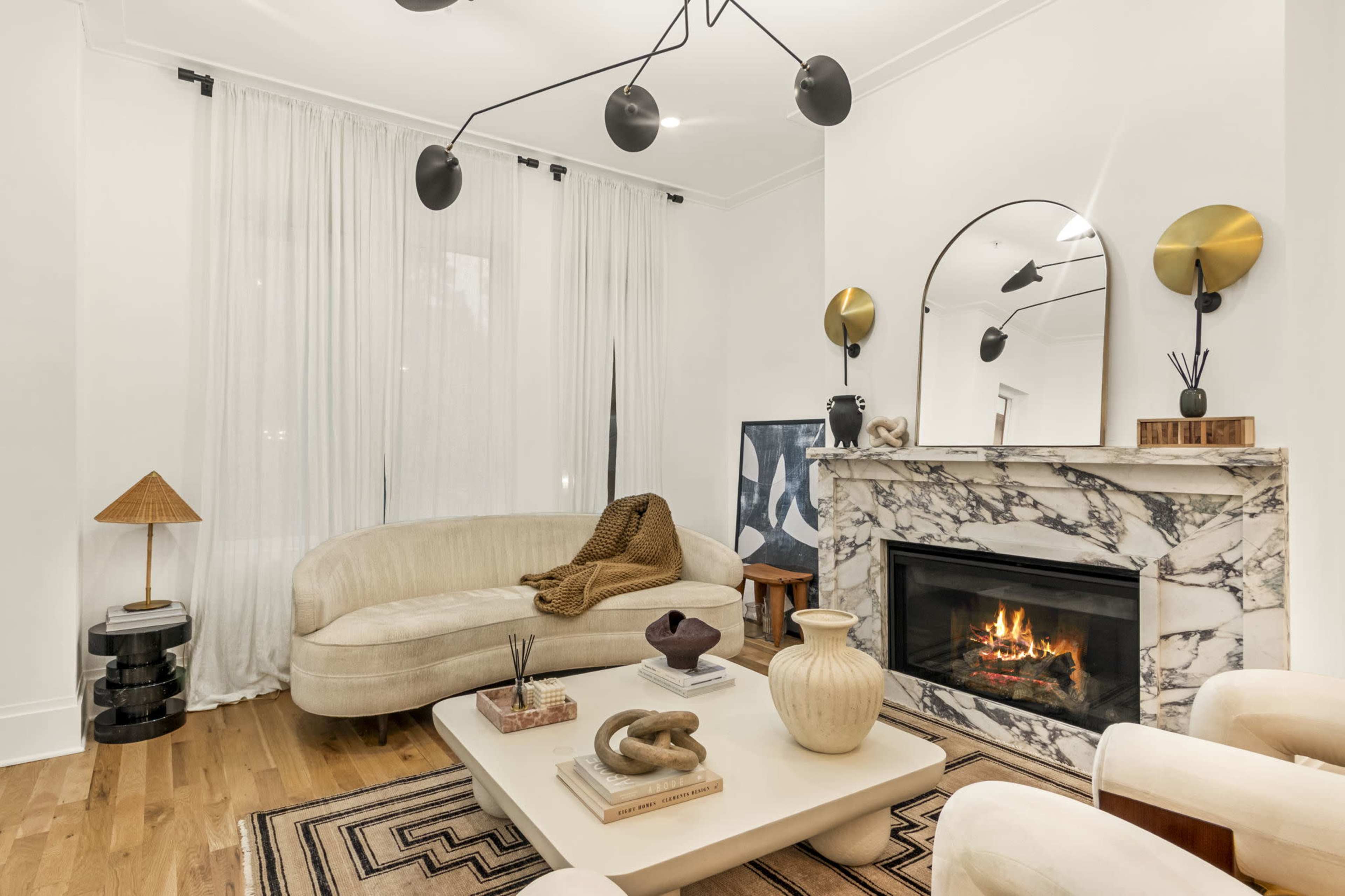 The image shows a modern living room featuring a light-colored sofa, a marbled fireplace, a coffee table, and decorative items on a hardwood floor.