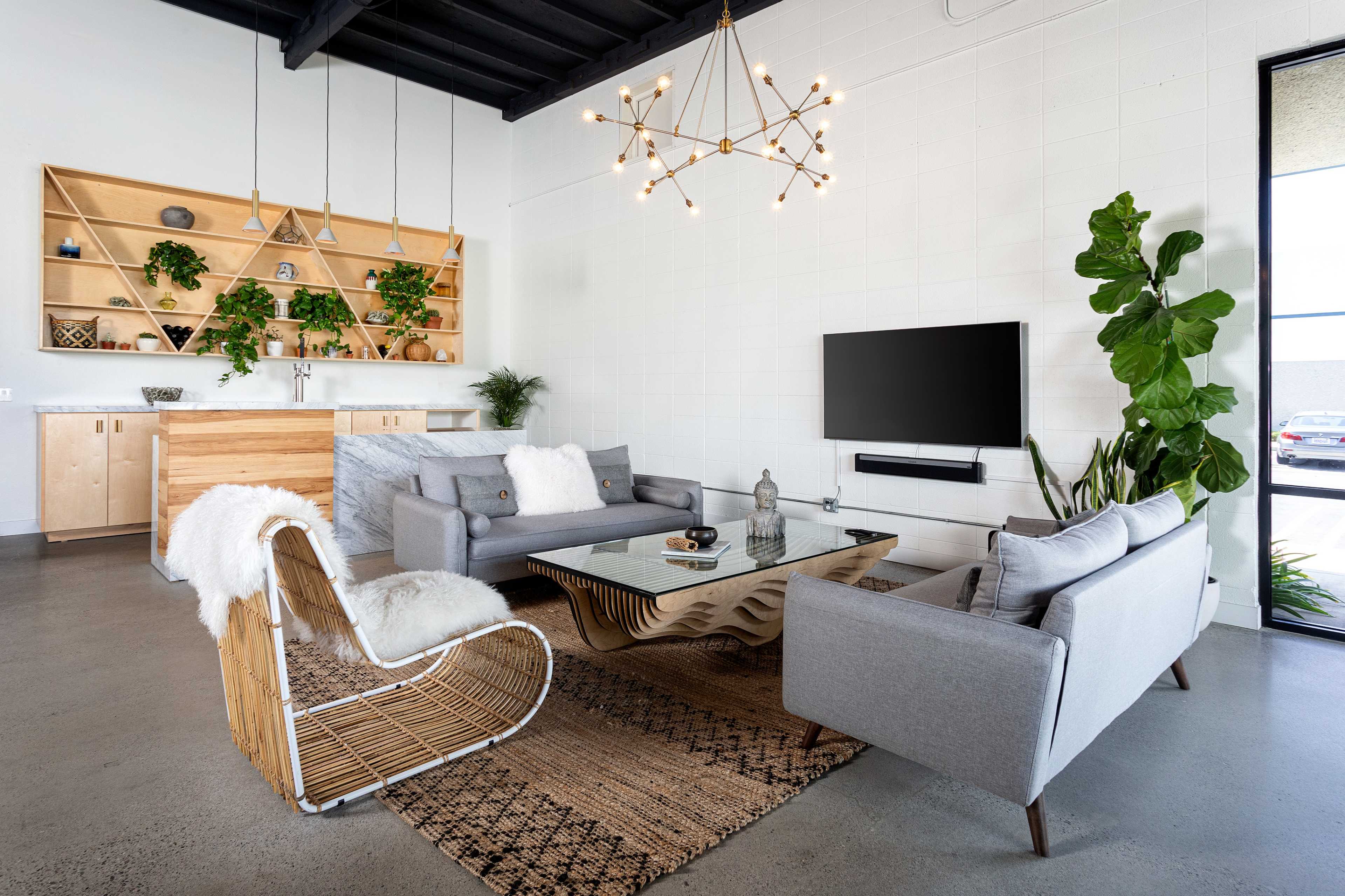 A modern living room with a gray sofa, a sculptural wooden coffee table, and a large window, featuring greenery and decorative shelves in the background.