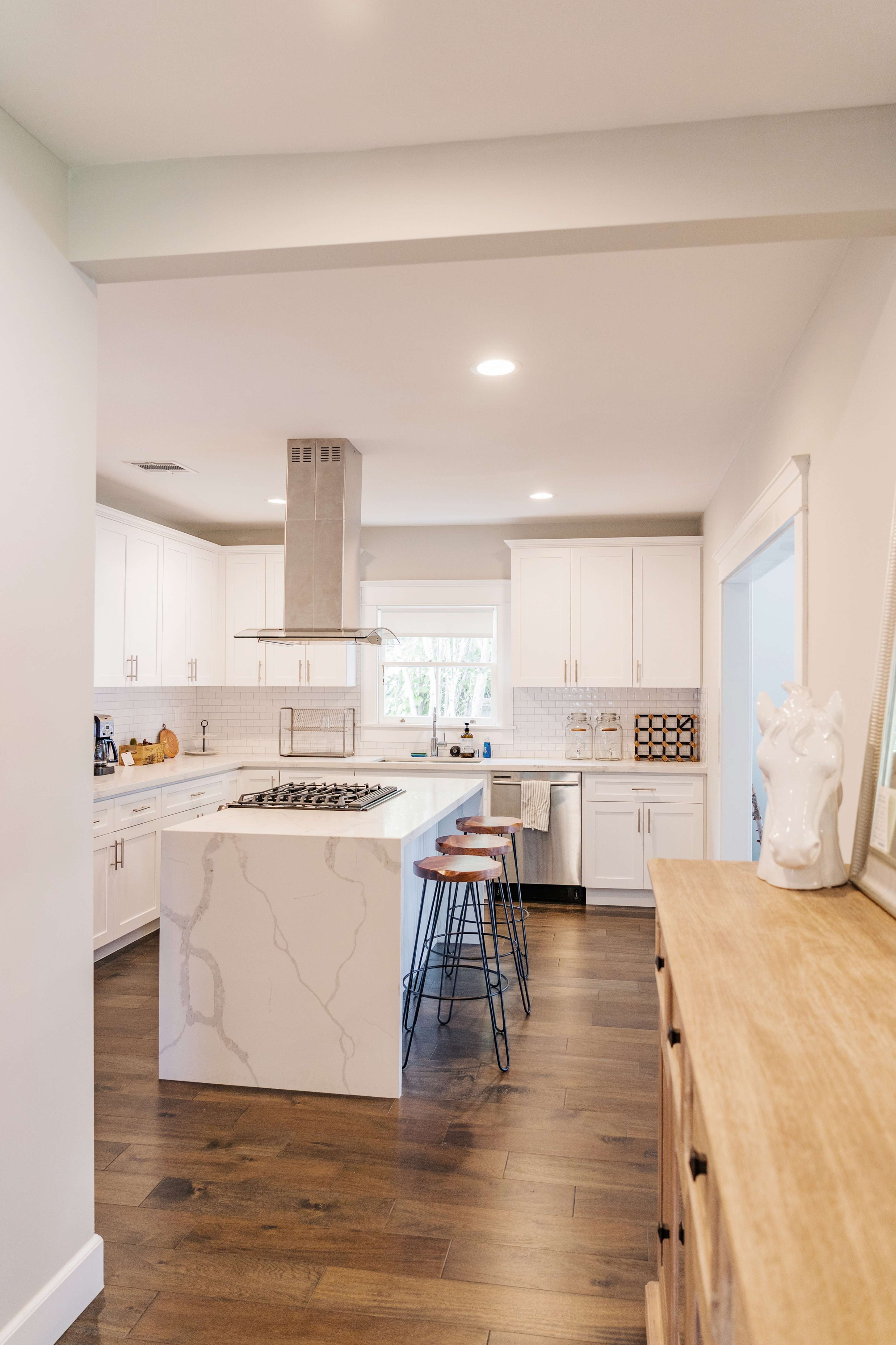 A modern kitchen features white cabinetry, a large island with a marble countertop, and hardwood flooring.