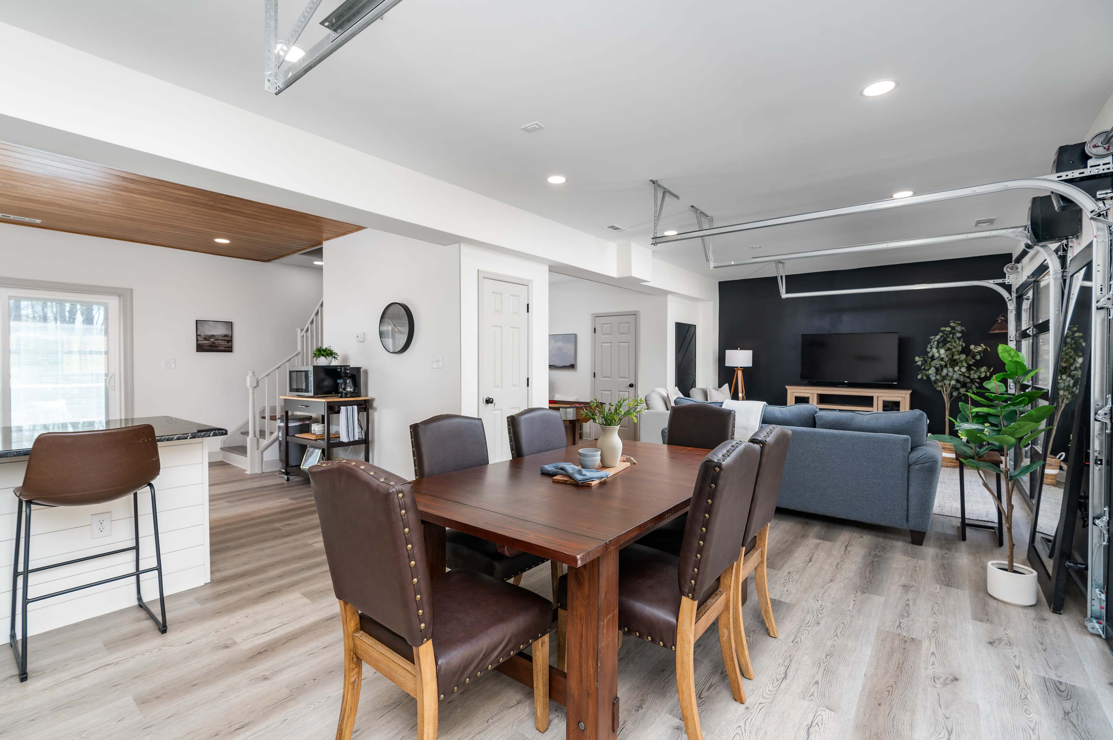 A modern open-concept living space with a dining area featuring a wooden table and leather chairs, adjacent to a living room with a sofa and a large television.