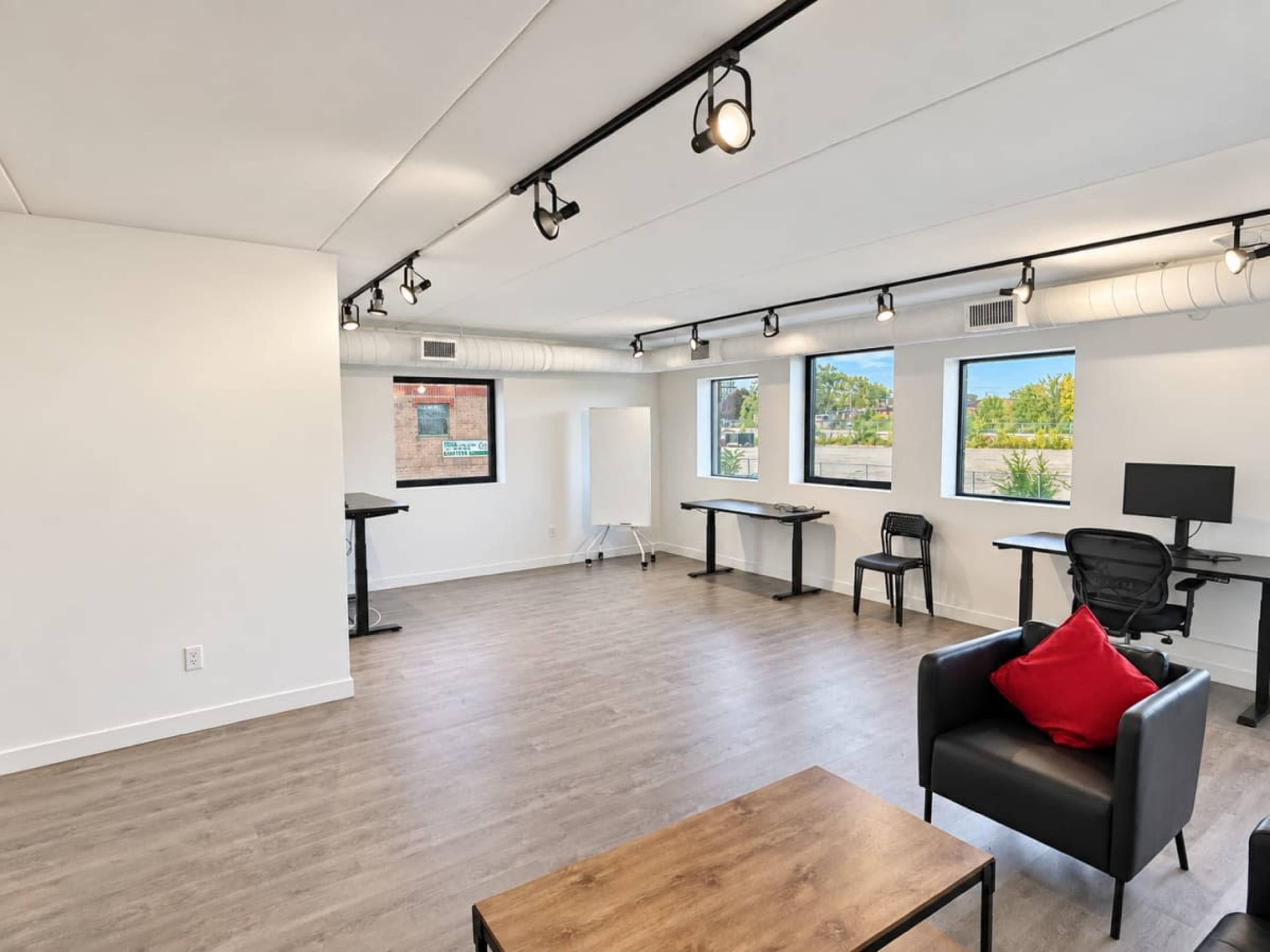 The image shows a modern, well-lit office space with three workstations and large windows allowing natural light.