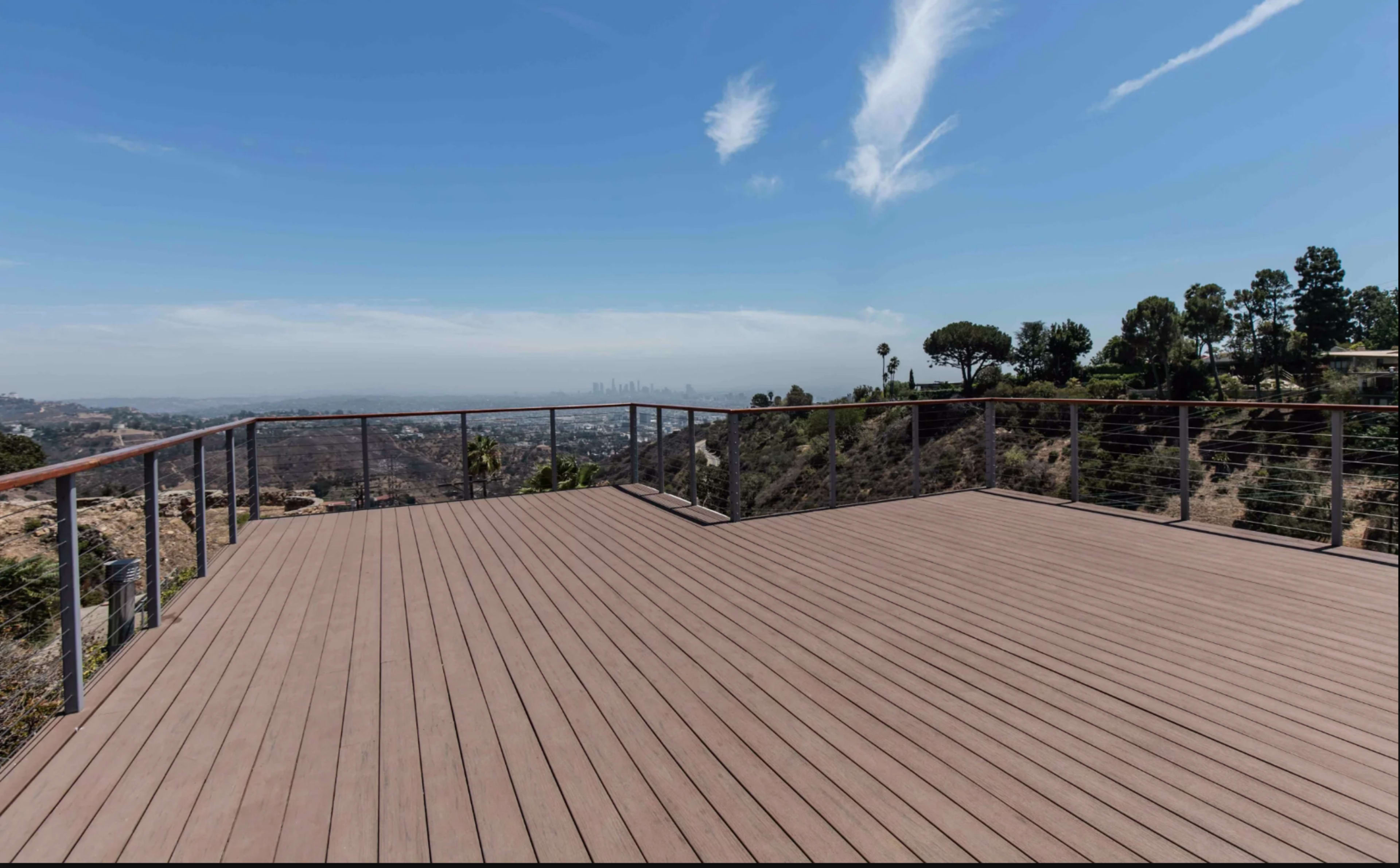 A spacious wooden deck overlooks a valley with distant city views under a clear blue sky.