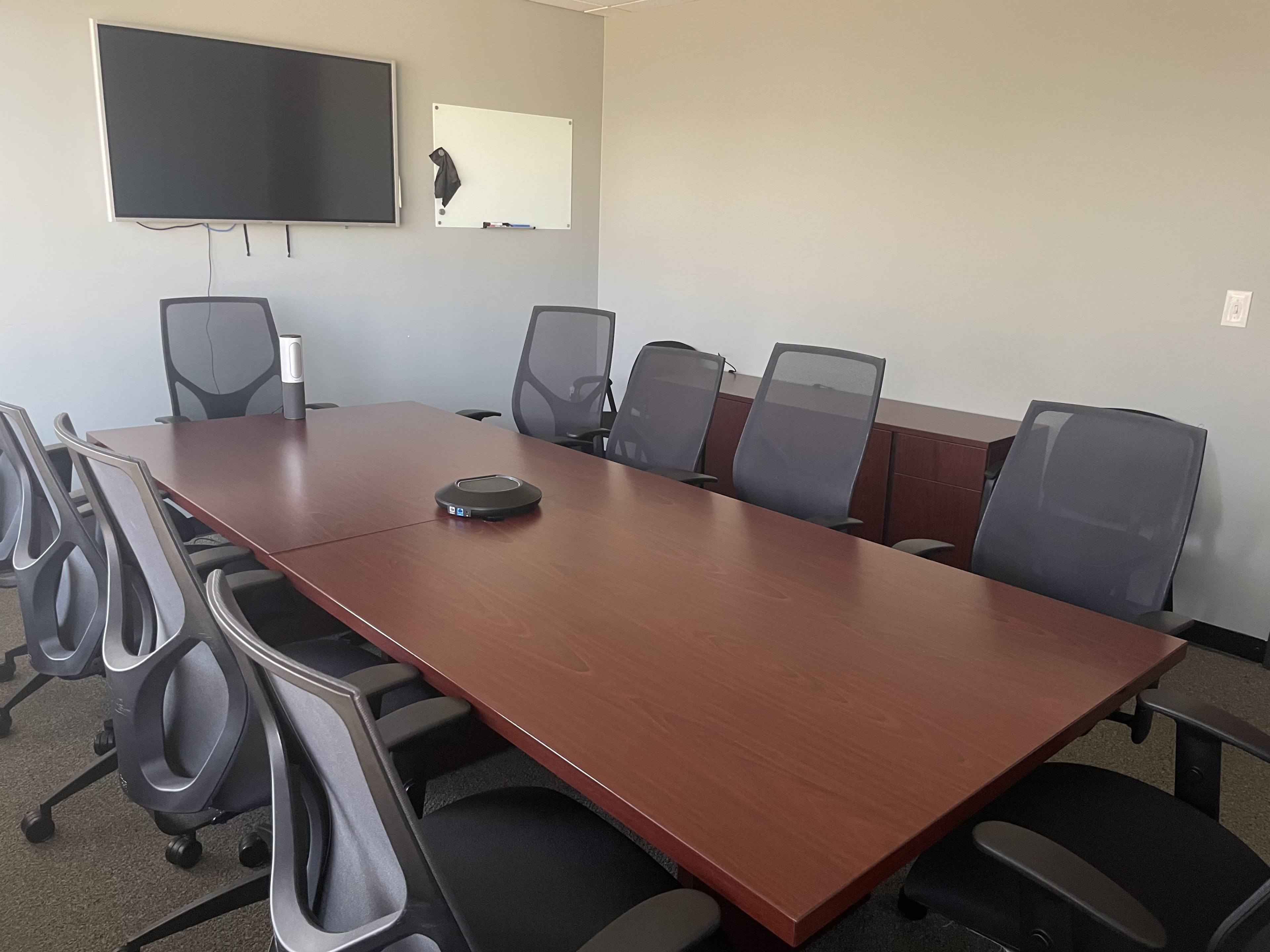 A conference room with a large wooden table surrounded by office chairs, a television mounted on the wall, and a whiteboard.