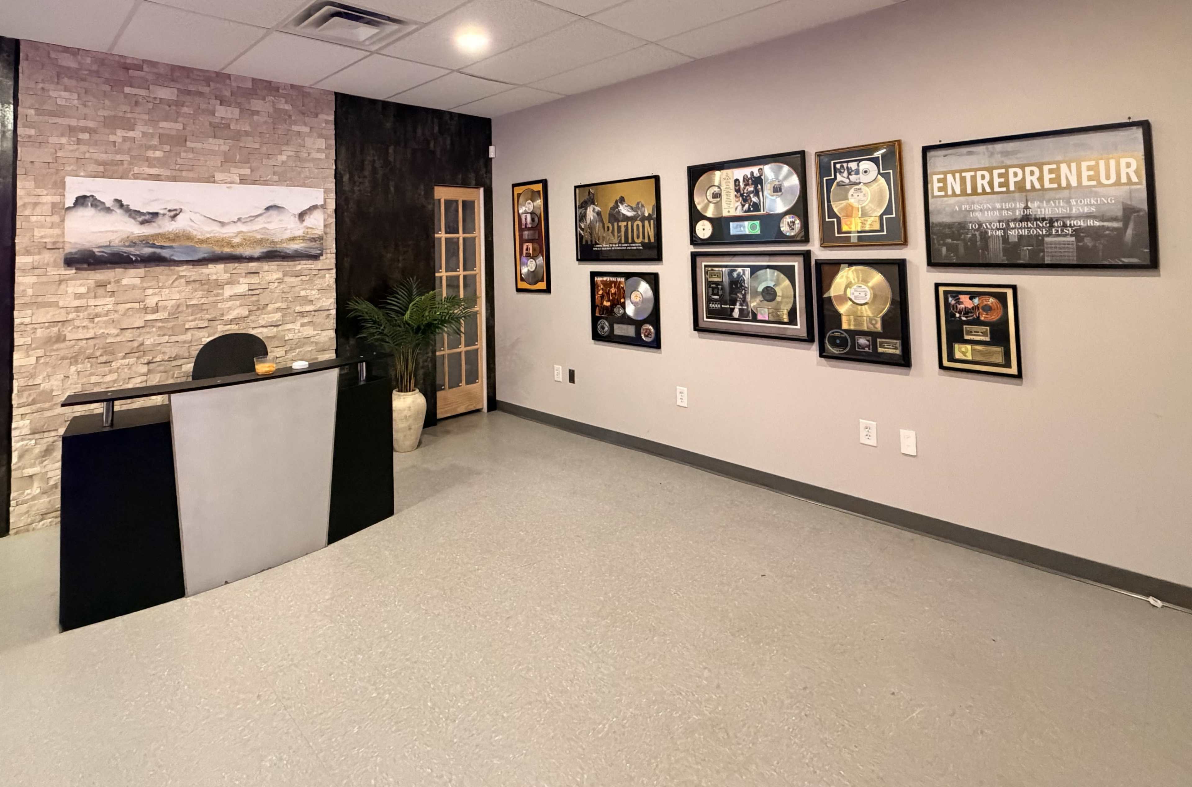 The image shows a modern reception area with a front desk, framed awards on the walls, and a decorative plant in the corner.