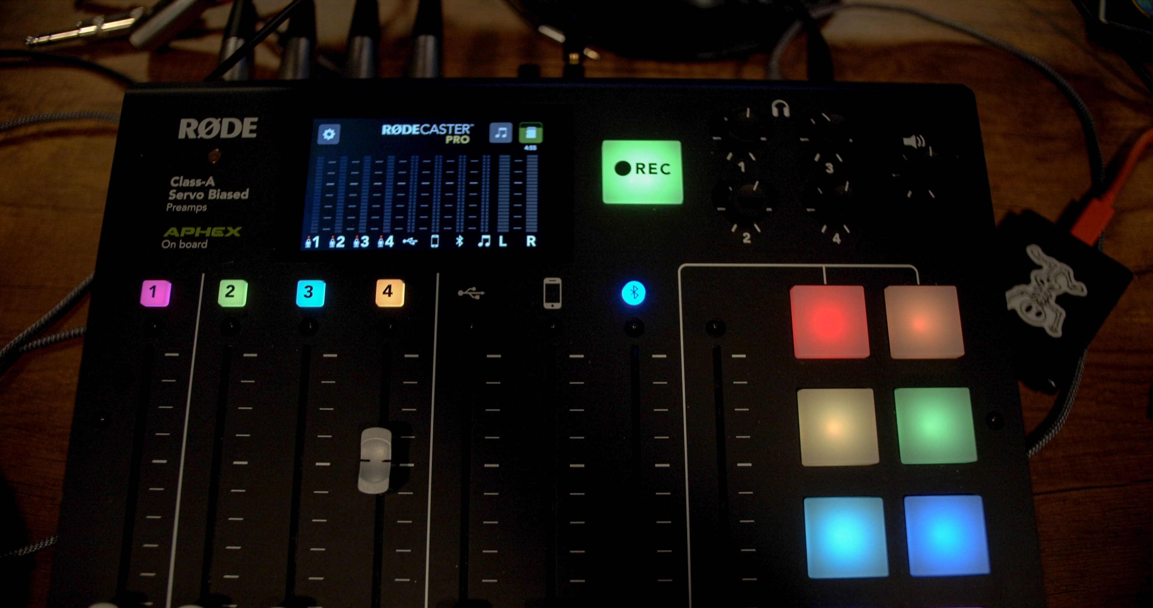 A close-up of a Rodecaster Pro audio mixer with various colored buttons and faders on a wooden surface.