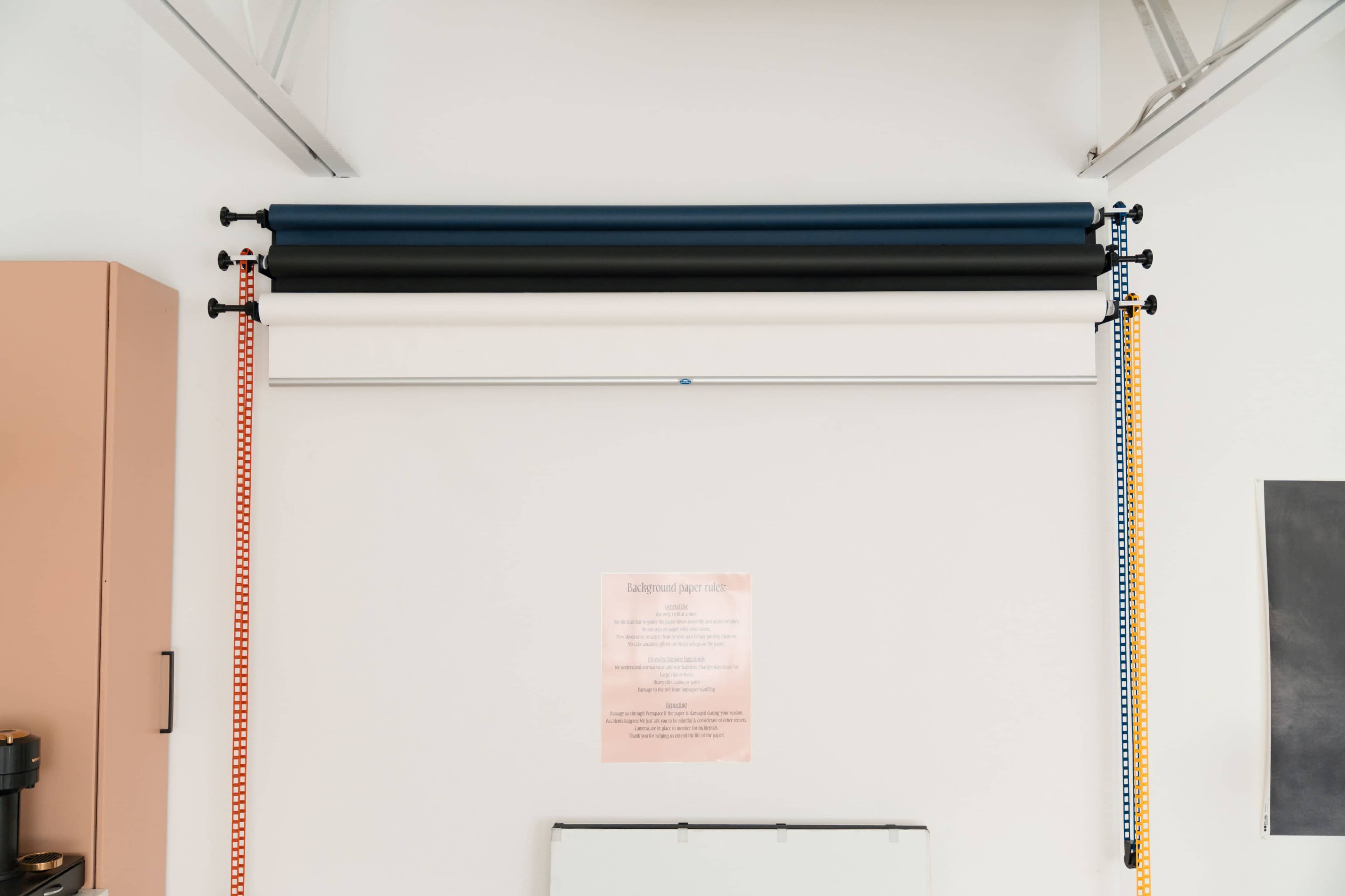 The image shows a wall with three rolled-up background fabric panels mounted above a notice posted on the wall.