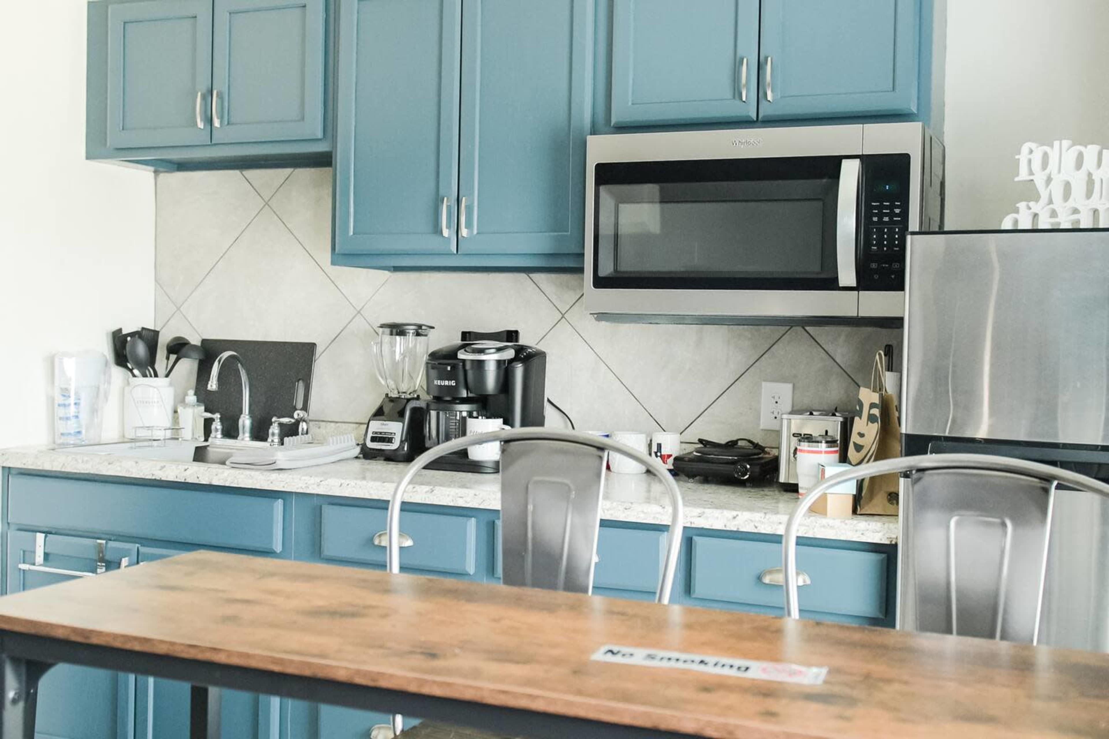 The image shows a modern kitchen with blue cabinets, a countertop, and various appliances including a microwave and a blender.