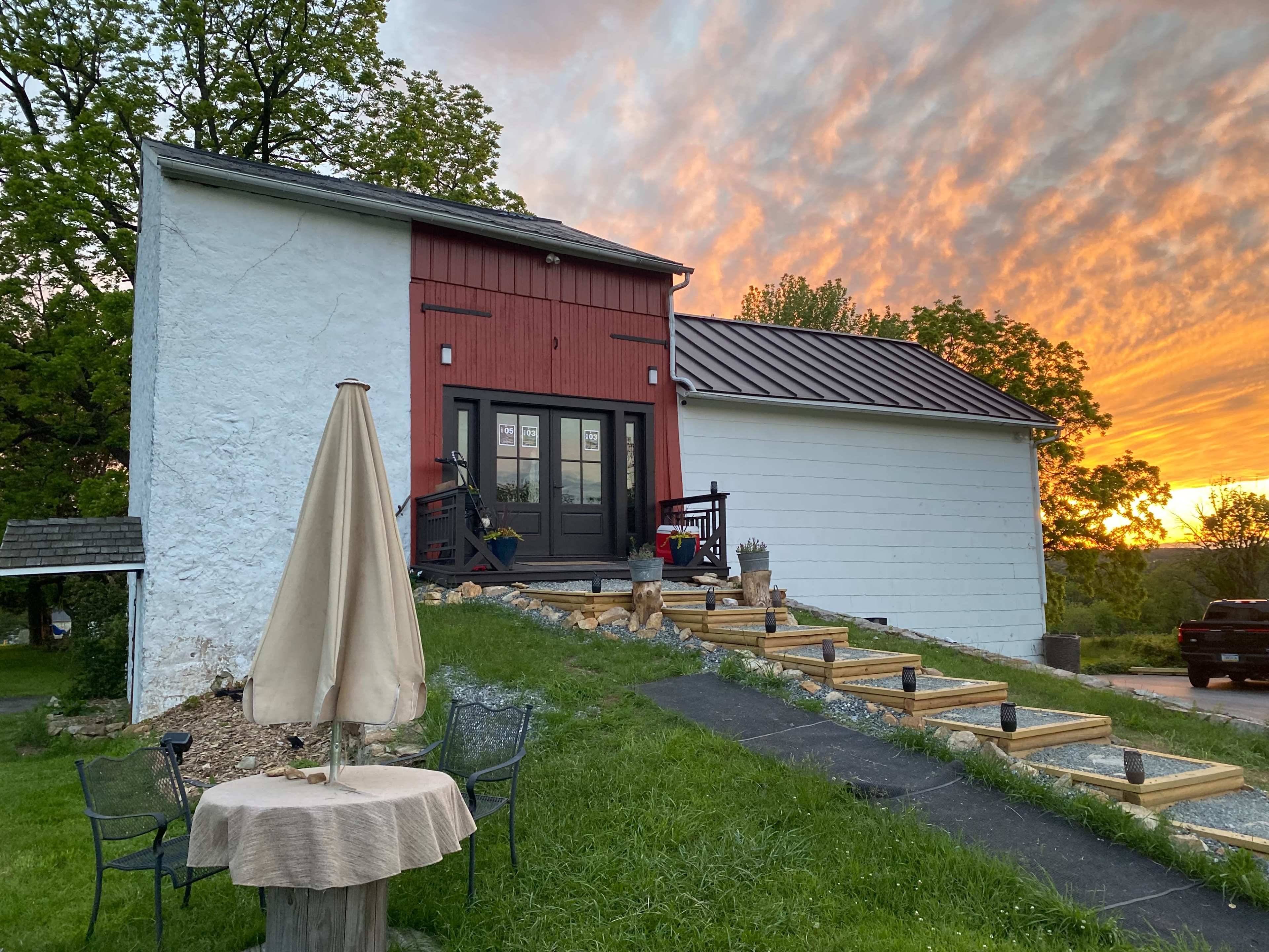 A house with a red and white exterior features a set of wooden steps leading to a door, set against a vibrant sunset.